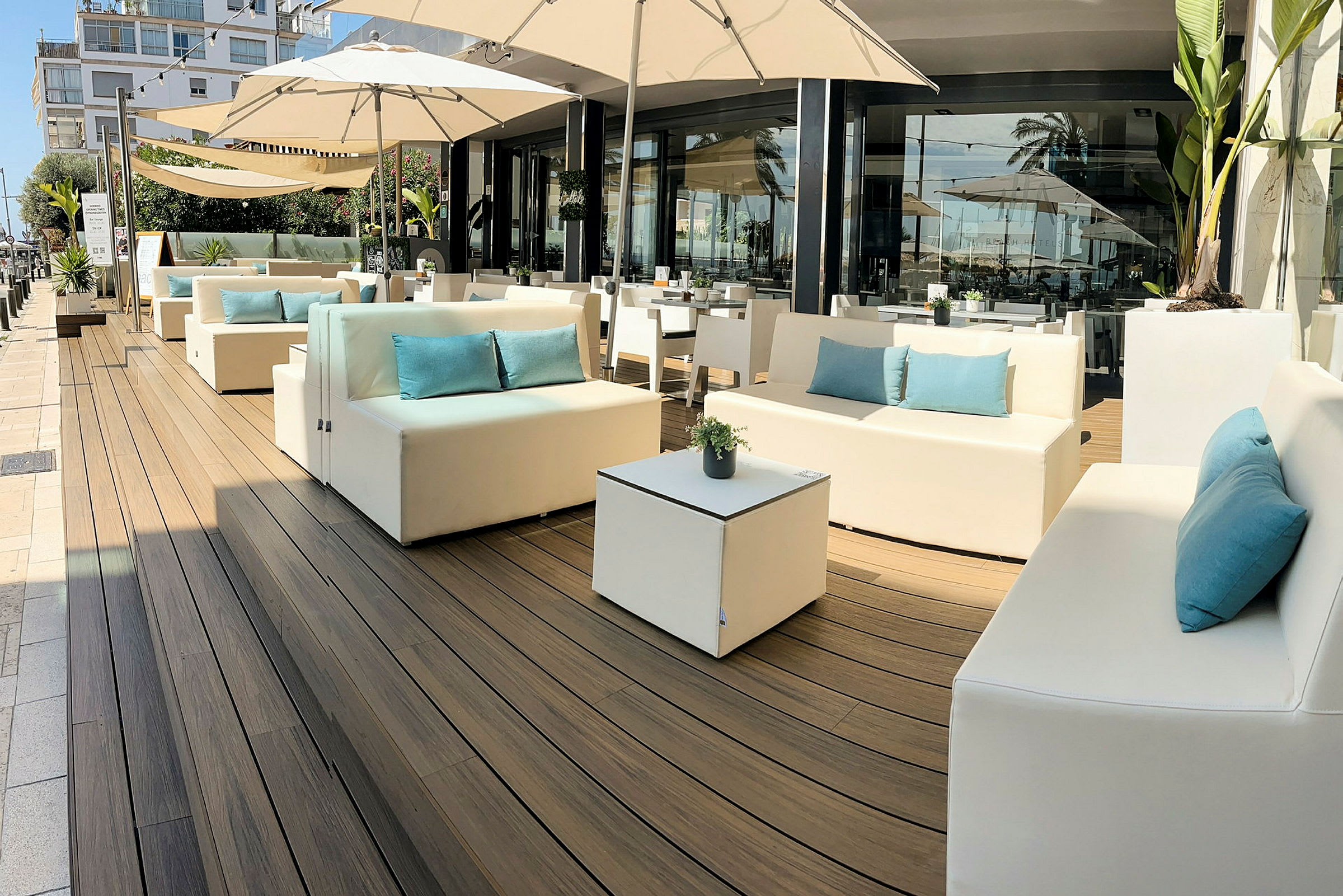Utendørs lounge med hvite sofaer, blå puter og parasoller. (AI-generert tekst)
