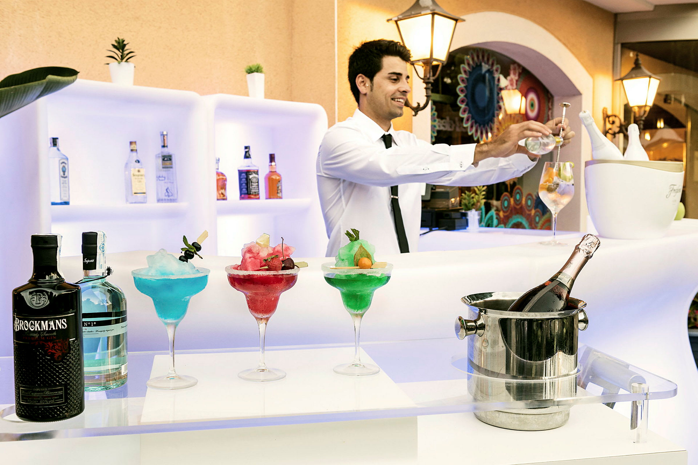 En bardisk med fargerike cocktails, flasker og en isbøtte med en flaske champagne. (AI-generert tekst)