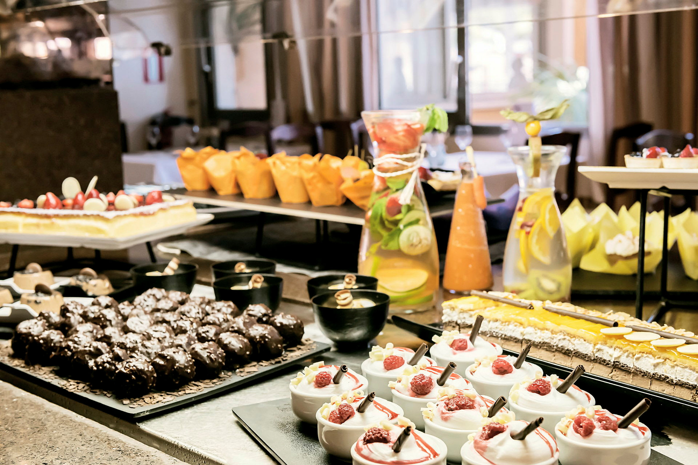 En dessertbuffé med ulike typer bakverk, mousse med bringebær, sjokolademuffins og en karaffel med sitronvann. (AI-generert tekst)