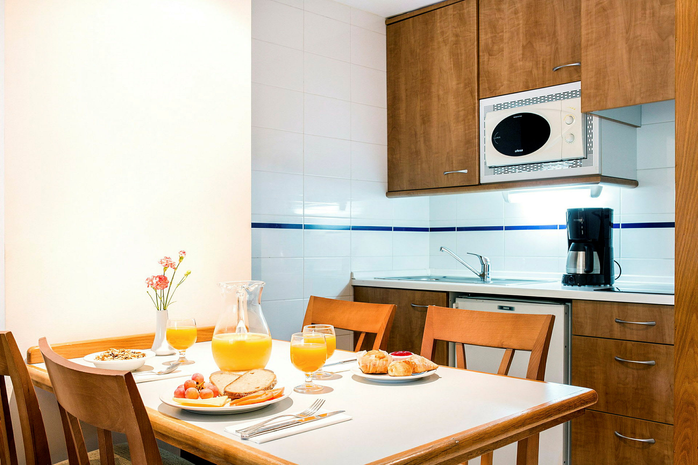 Et bilde av et kjøkken med et trebord dekket for frokost samt en oppvaskkum og kjøkkenskap i bakgrunnen. (AI-generert tekst)