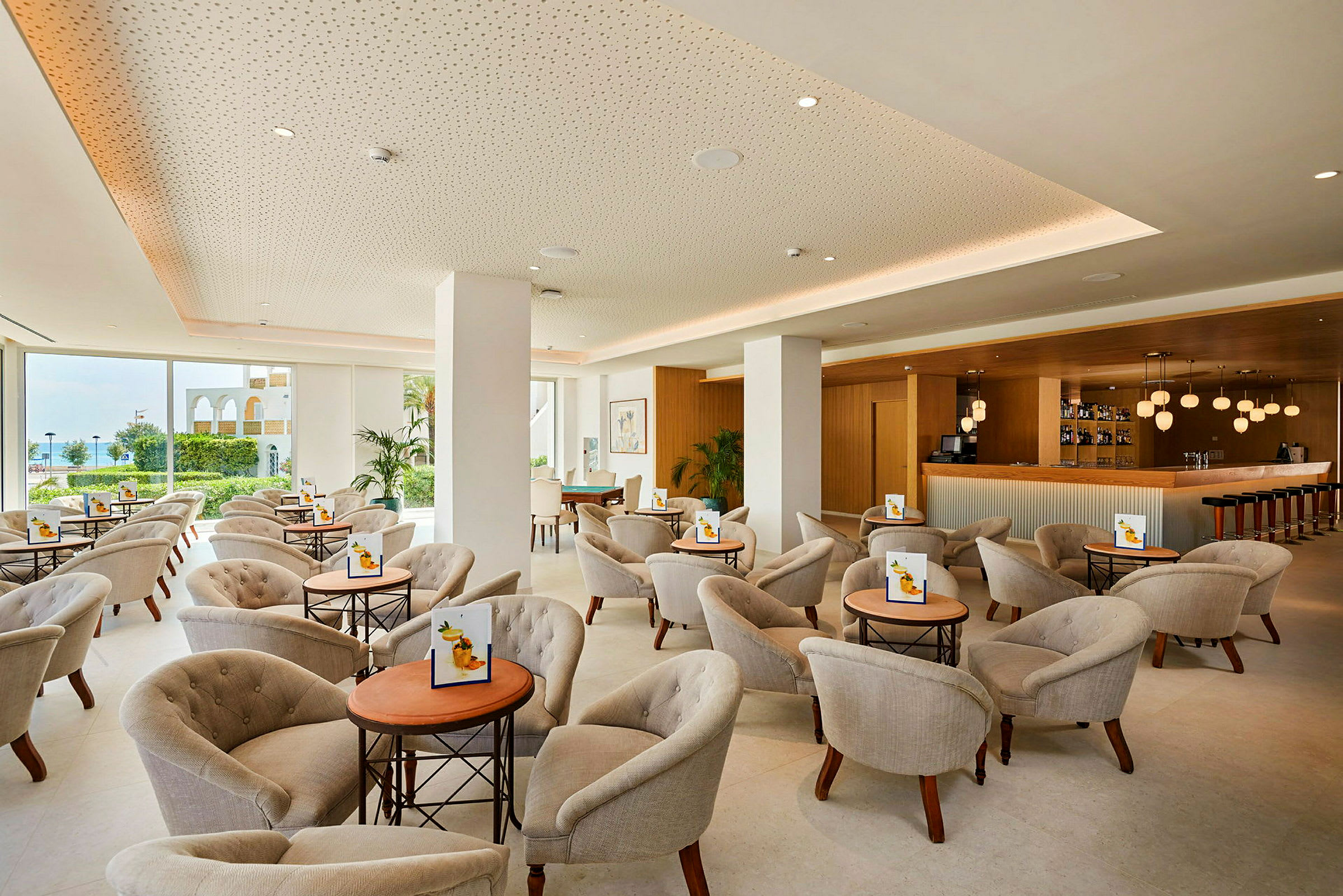 Lys og moderne lounge med stoler og små bord, samt en bardisk. (AI-generert tekst)