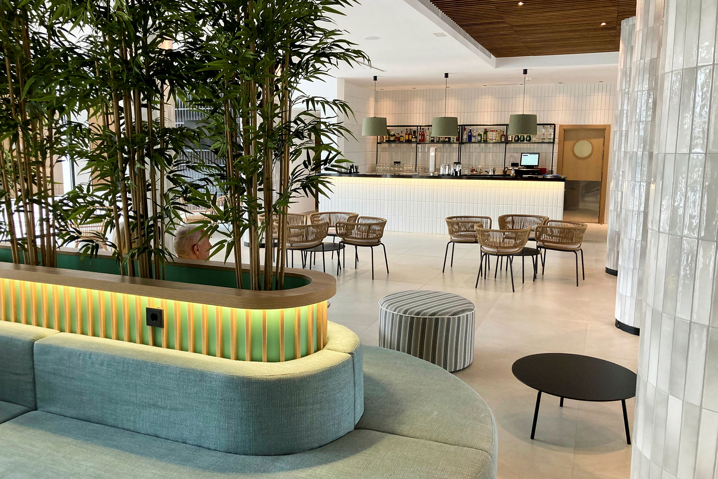 Interiøret i en moderne lounge med grønne planter, sittemøbler og en bar i bakgrunnen. (AI-generert tekst)
