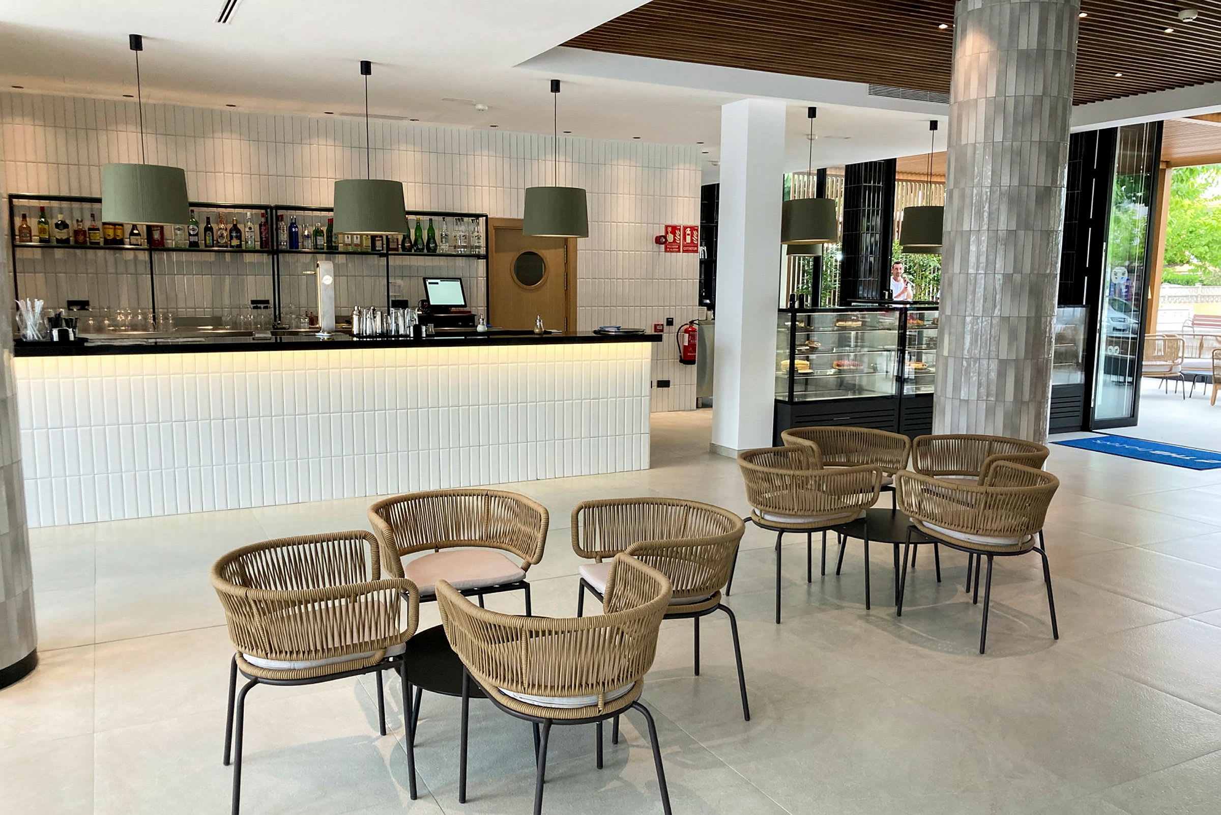 Bilde av en moderne lounge med en bar, bord og stoler samt et glassmonter med bakverk. (AI-generert tekst)