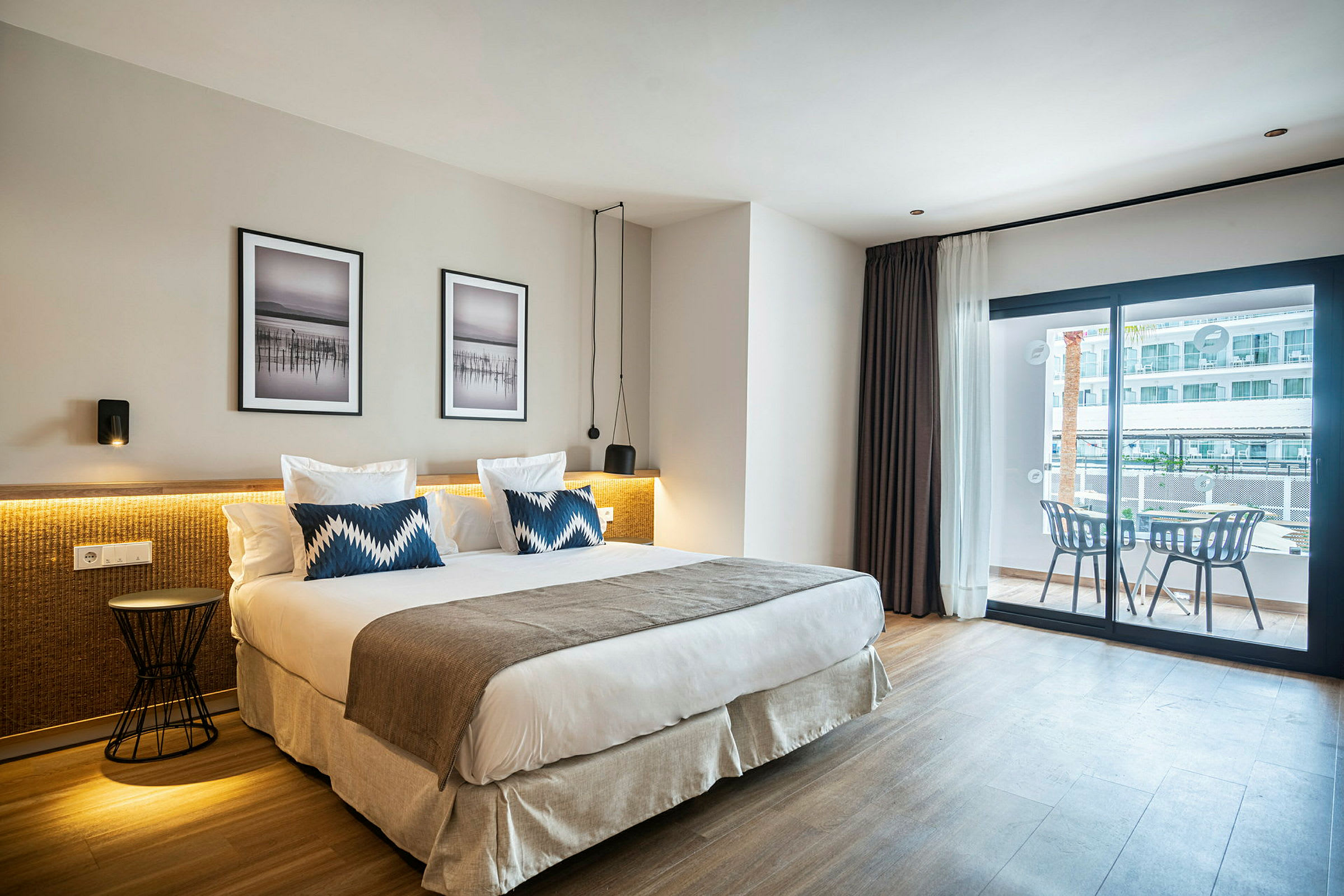 Hotellrom med en stor seng, to puter og moderne innredning, samt en balkong med sittemøbler. (AI-generert tekst)