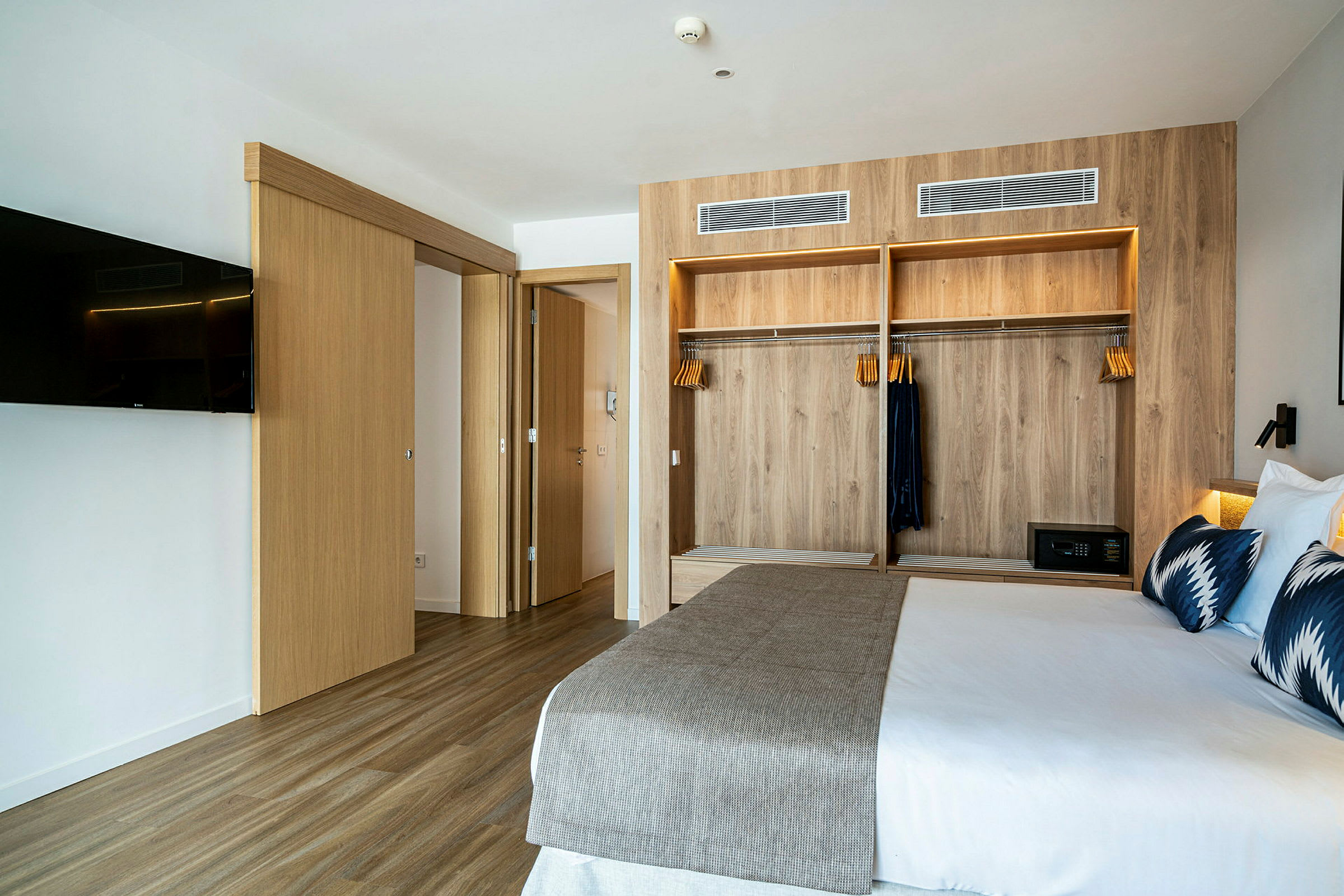 Et moderne hotellrom med en seng, en garderobe med trepanel og en veggmontert TV. (AI-generert tekst)