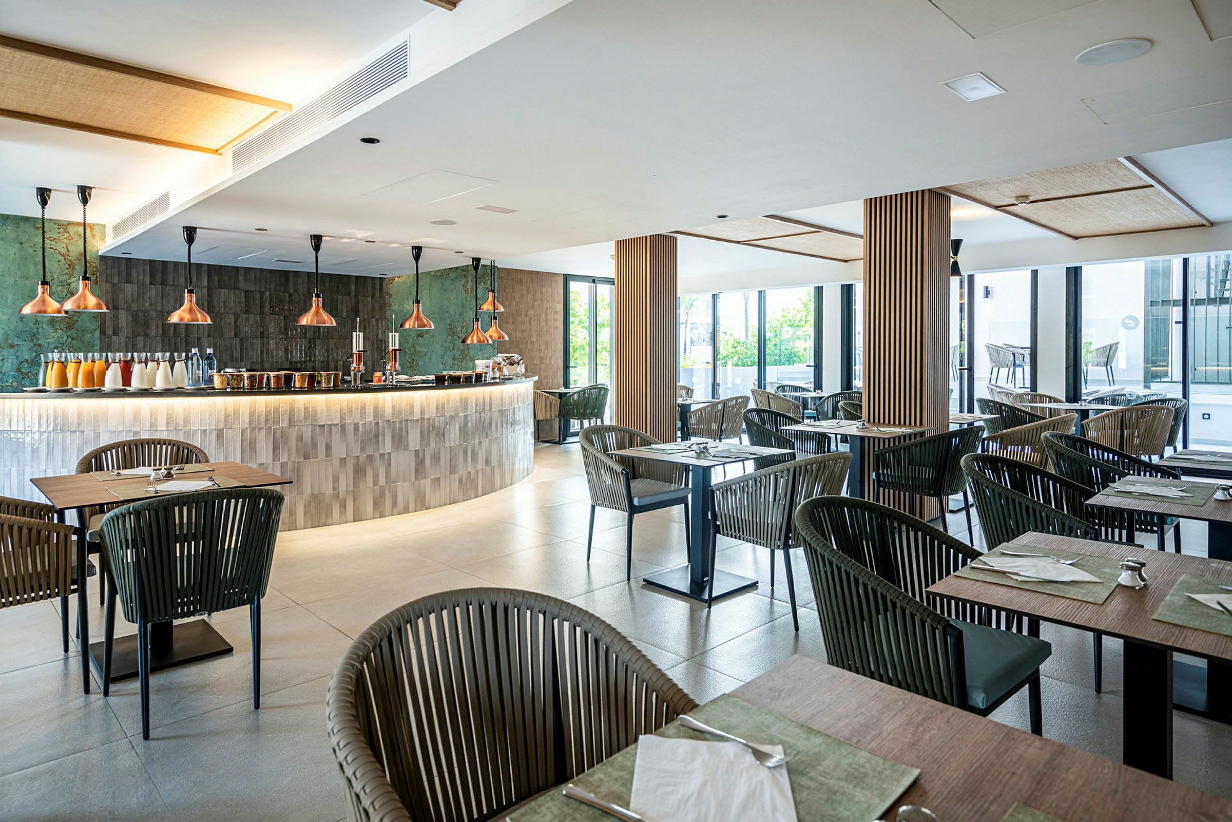 Bilde av en moderne restaurant med bord og stoler i tre og metall, samt en elegant bardisk med kobberlamper. (AI-generert tekst)