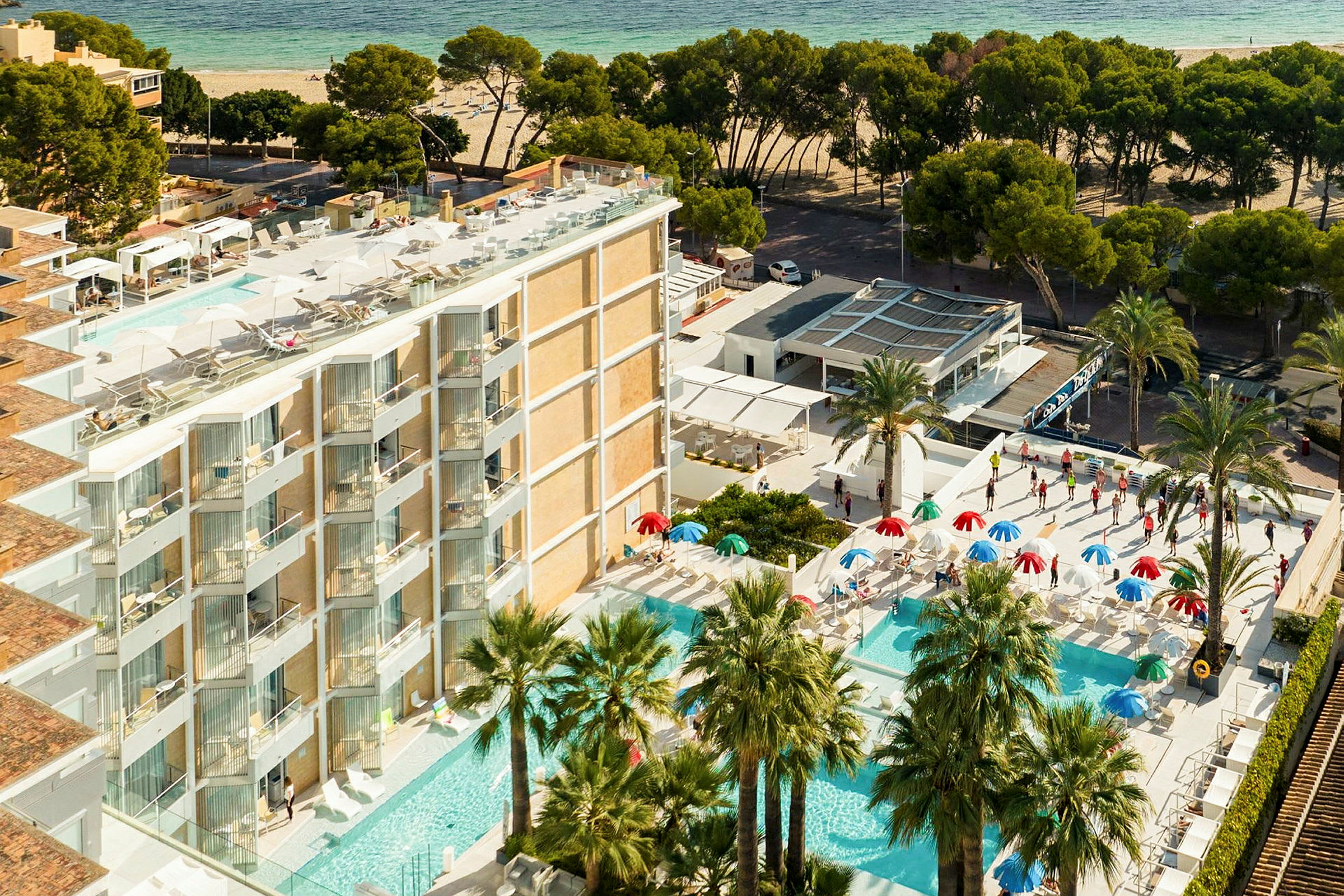 Utsikt over hotellområde med flere bassenger, parasoller og palmer nær en sandstrand. (AI-generert tekst)