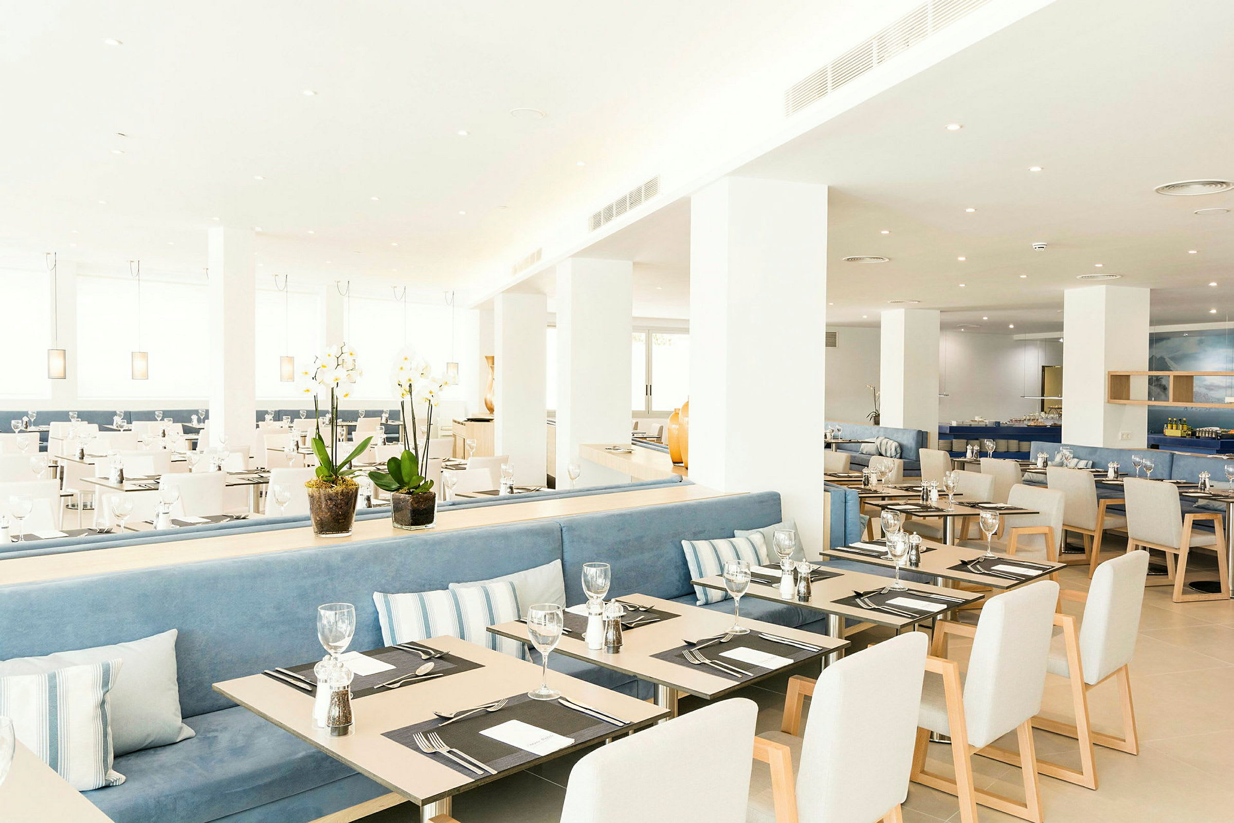 Et moderne og lyst innredet restaurantområde med dekkede bord og stoler. Planter på bordet tilfører et dekorativt preg. (AI-generert tekst)
