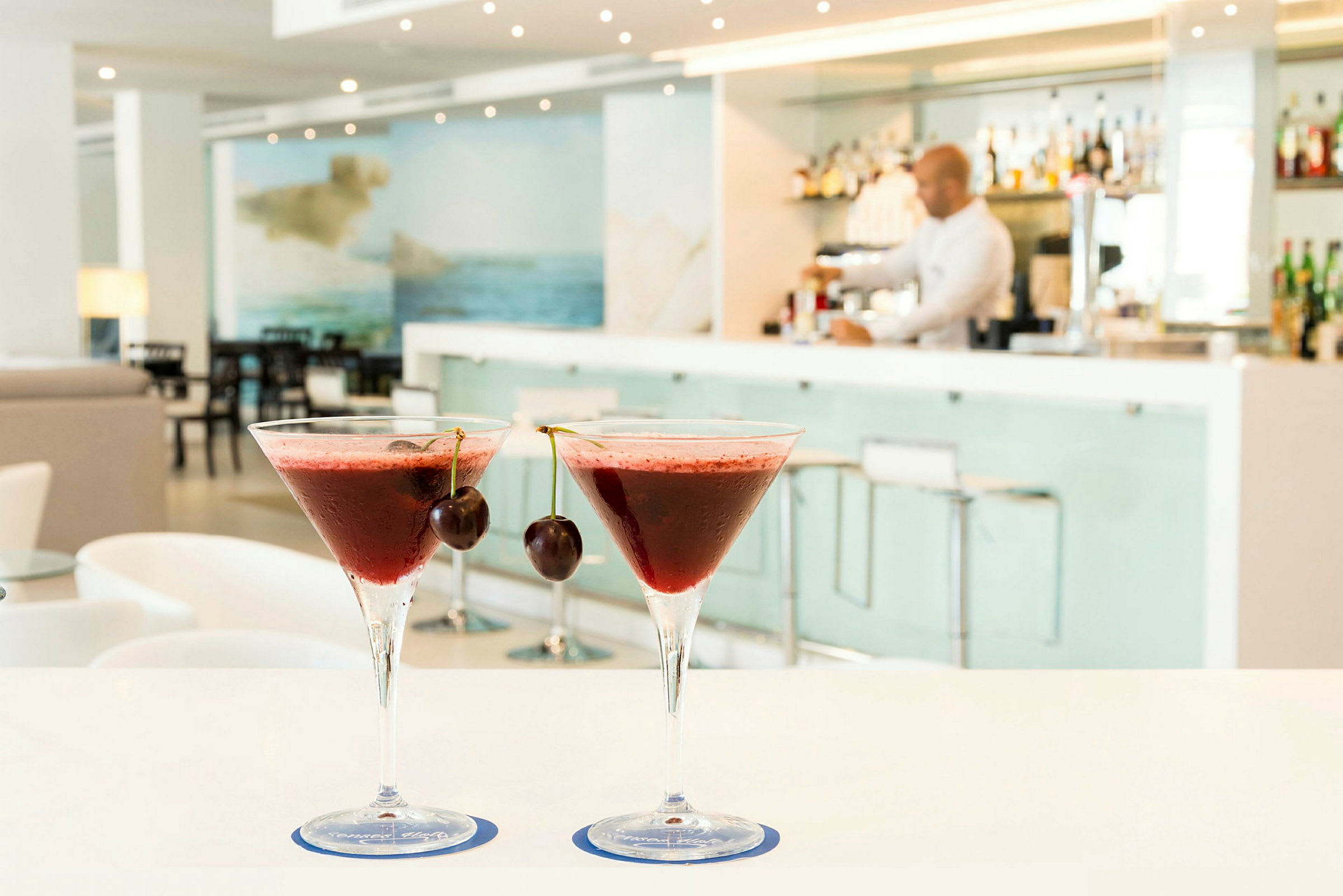 To røde cocktails med kirsebær på toppen står på et bord i en moderne bar. (AI-generert tekst)