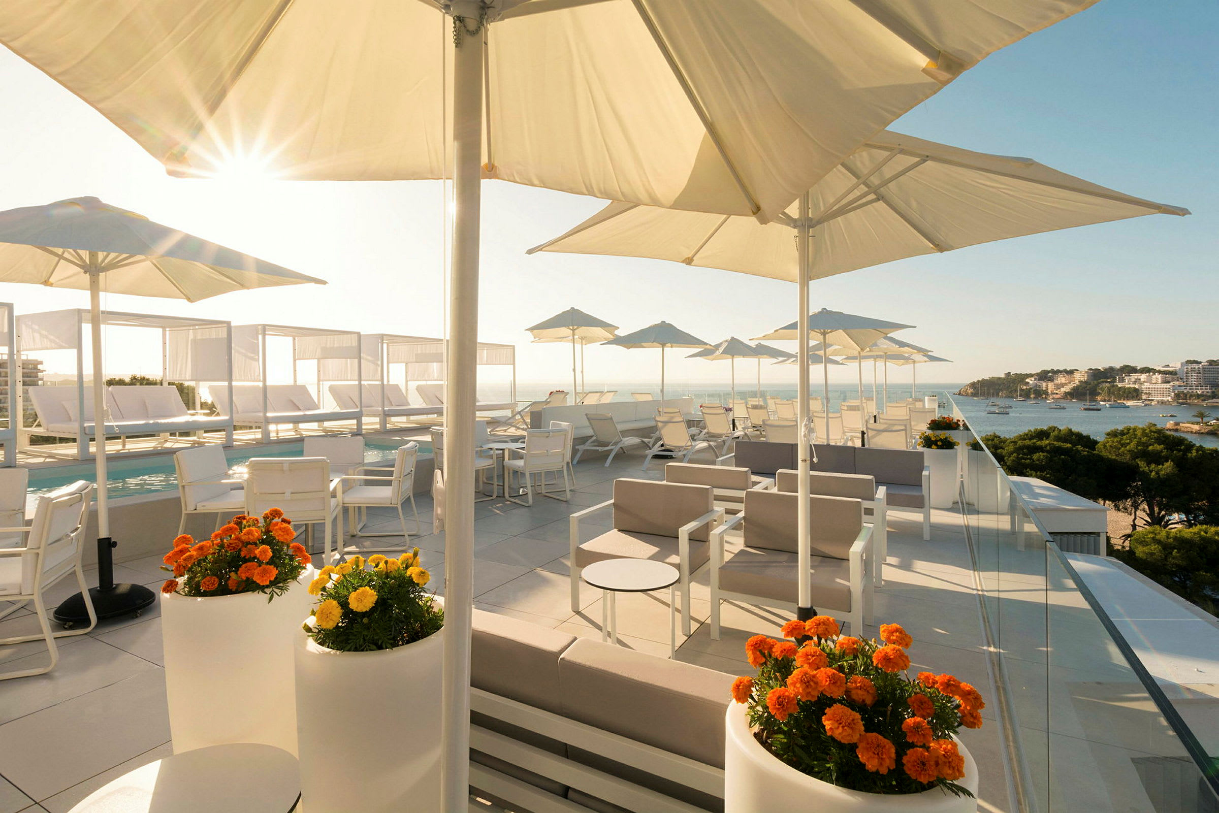 Takterrasse med solsenger og parasoller samt utsikt over havet og omkringliggende landskap. (AI-generert tekst)