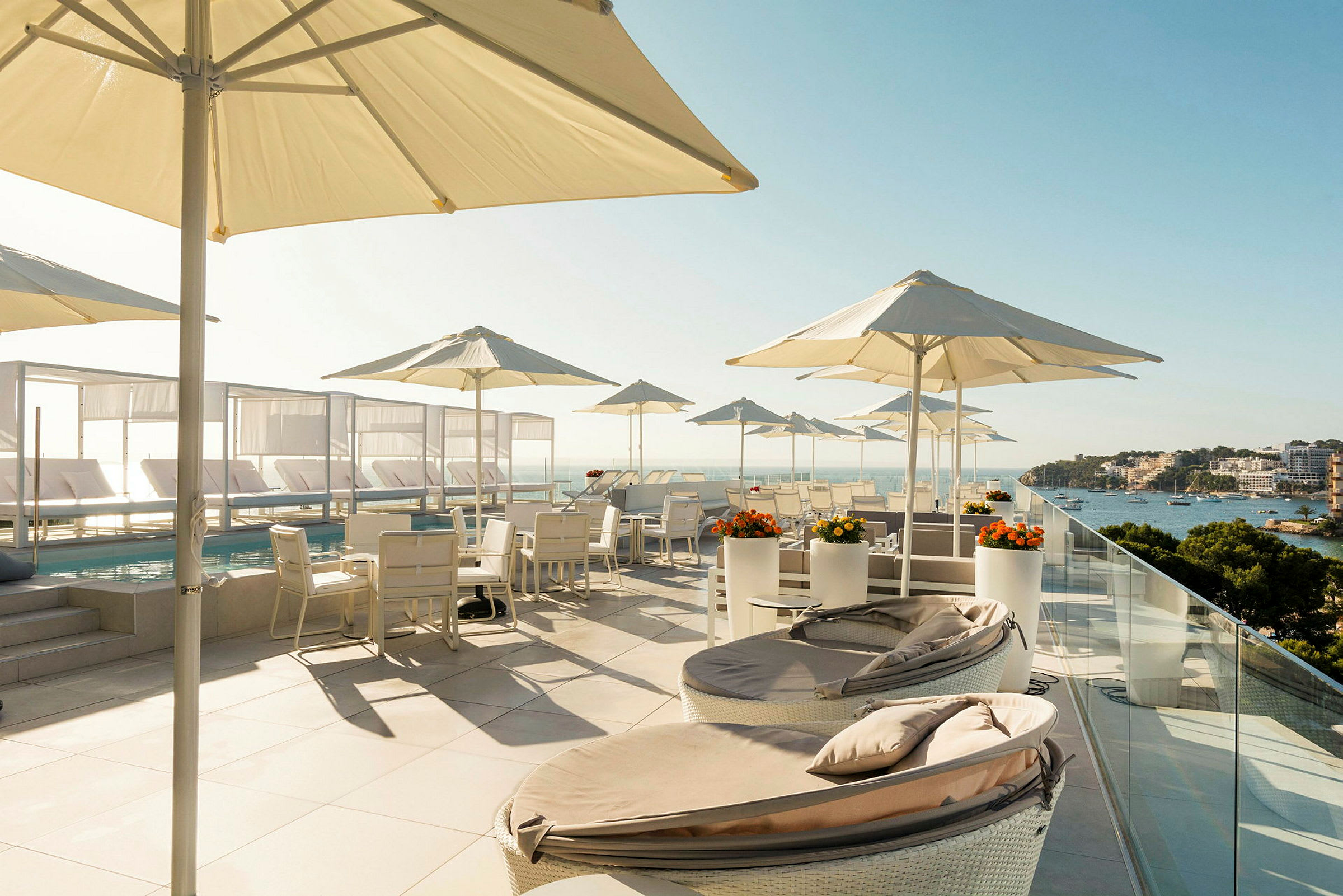 En takterrasse med solsenger, parasoller og sitteplasser ved et bord. Utsikt over havet og nærområdet. (AI-generert tekst)