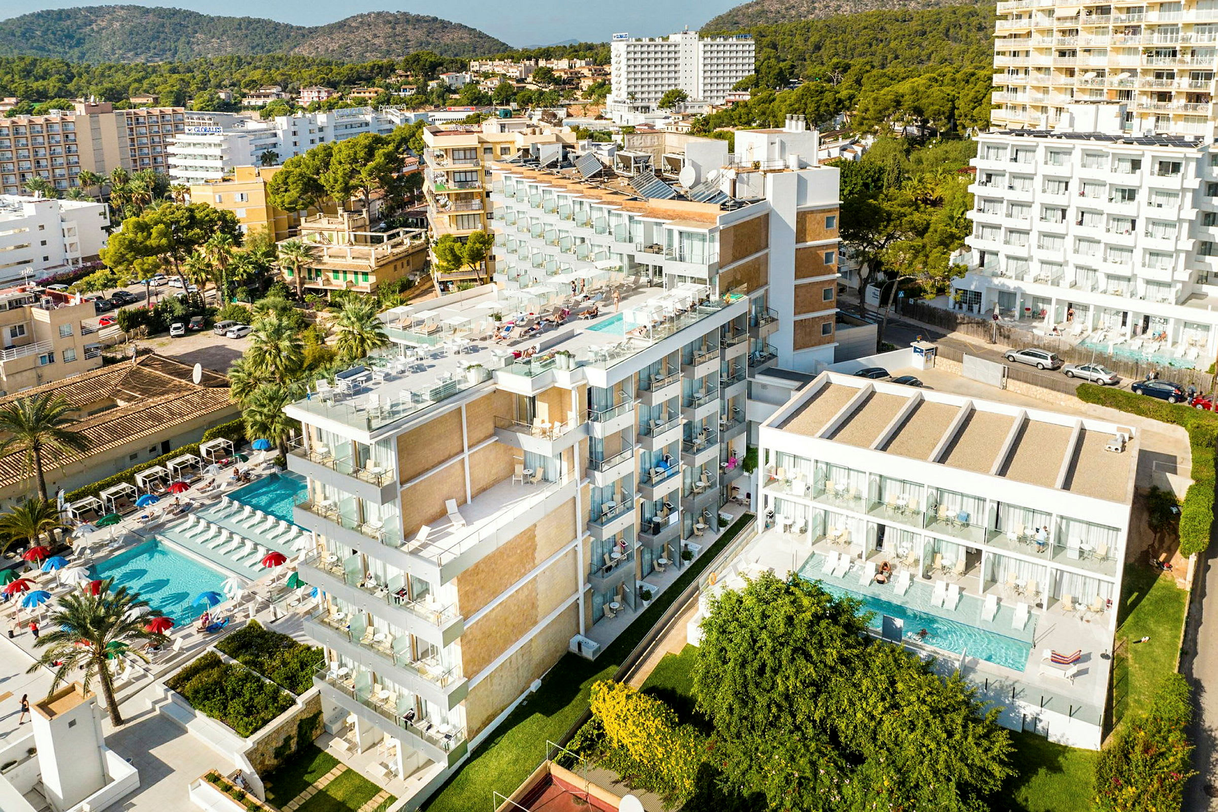 Bilde av et hotellkompleks med bassengområde og omkringliggende bygninger, omgitt av grøntområder og kupert terreng. (AI-generert tekst)