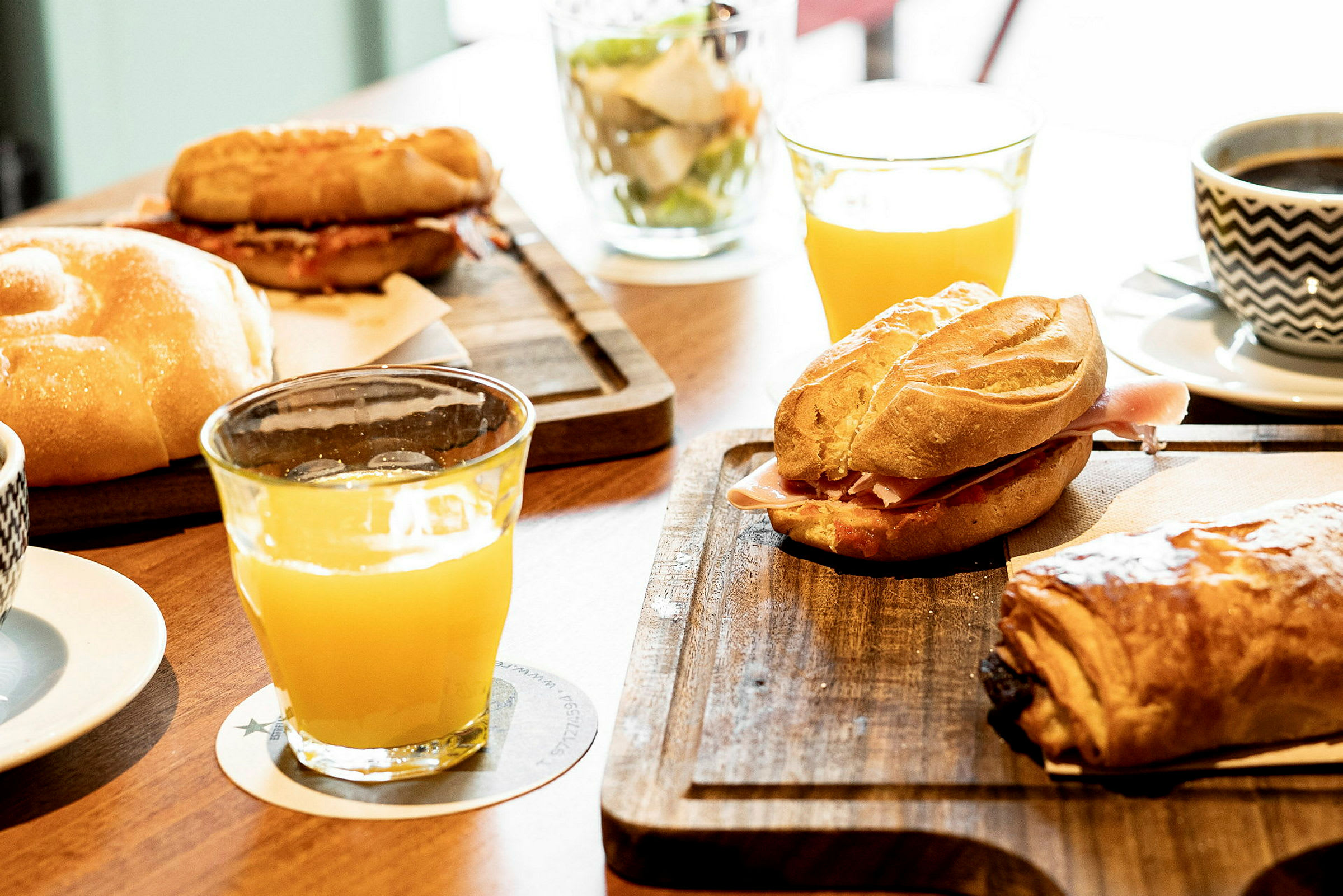Bildet viser en frokostservering med brød, croissanter, appelsinjuice og kaffe på bordet. (AI-generert tekst)
