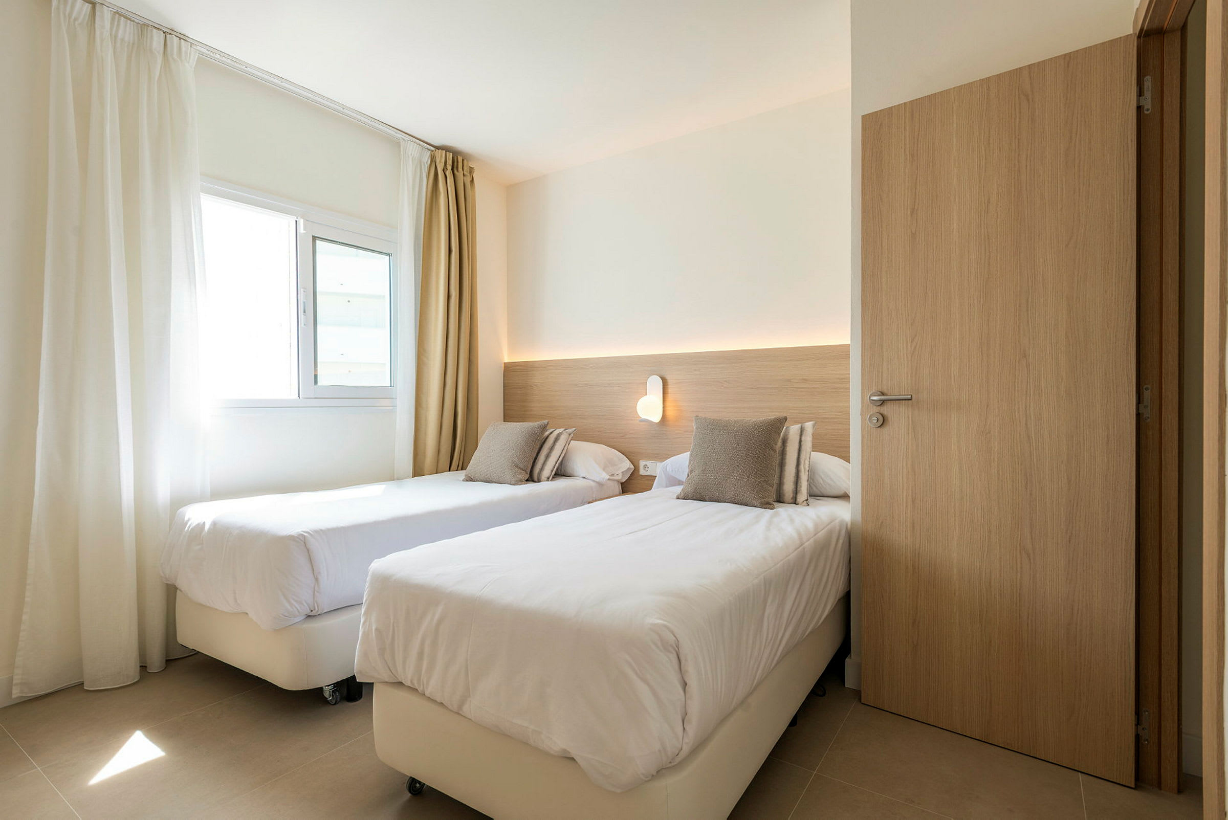 Hotellrom med to enkeltsenger og en vegglampe. (AI-generert tekst)
