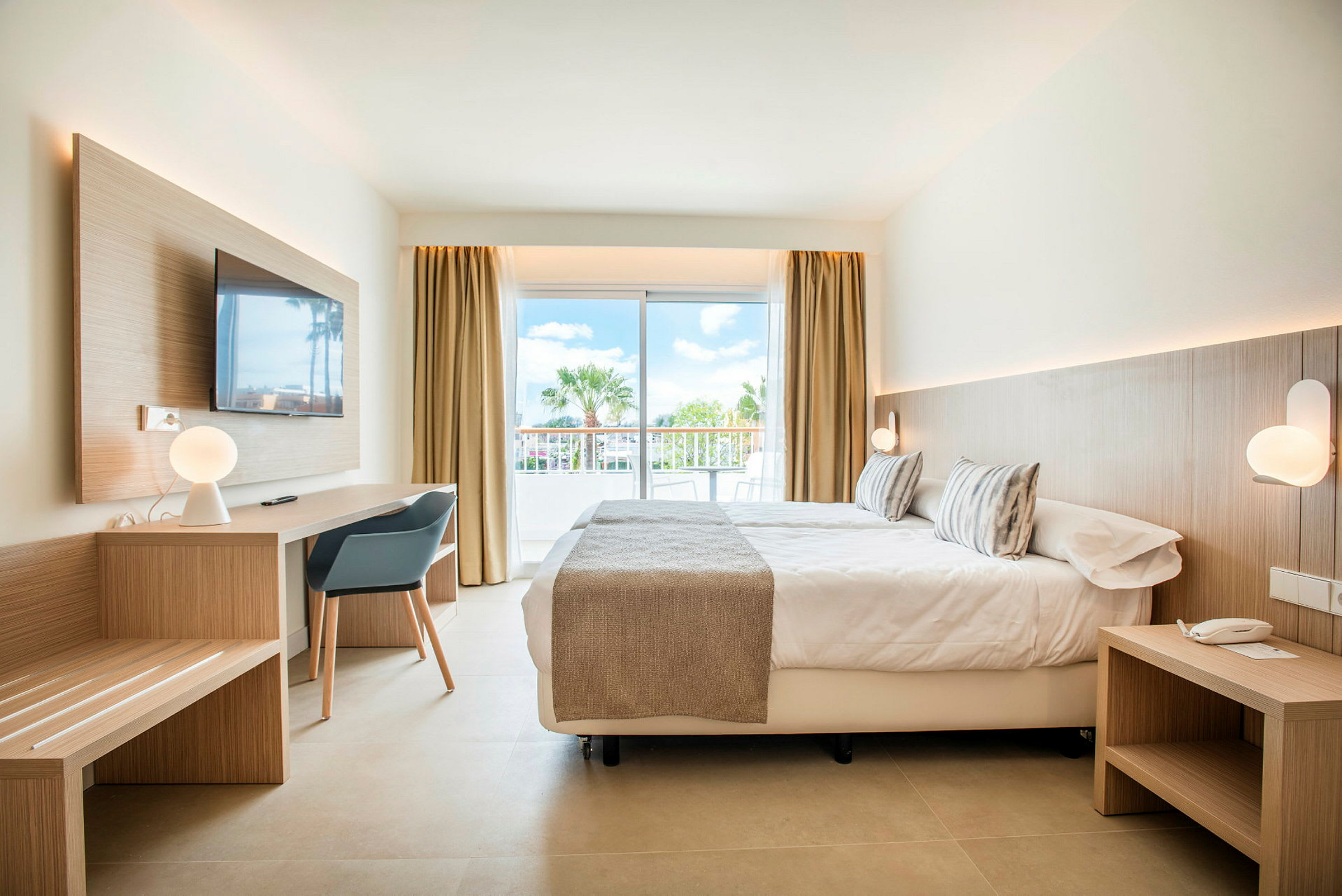 Moderne innredet hotellrom med seng, skrivebord og store glassdører mot en balkong. (AI-generert tekst)