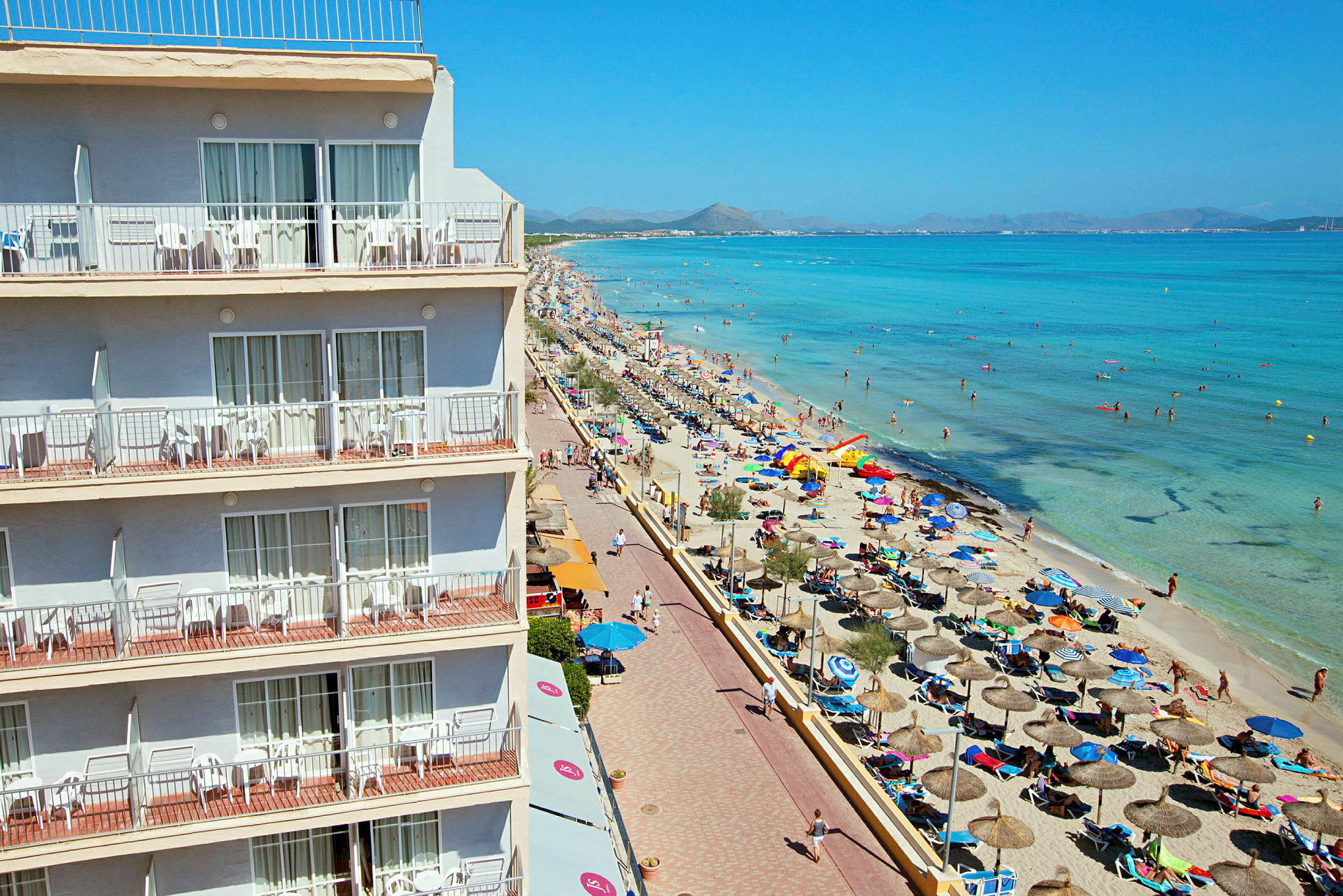 Hotell med balkonger ved en livlig strand og klart hav. (AI-generert tekst)