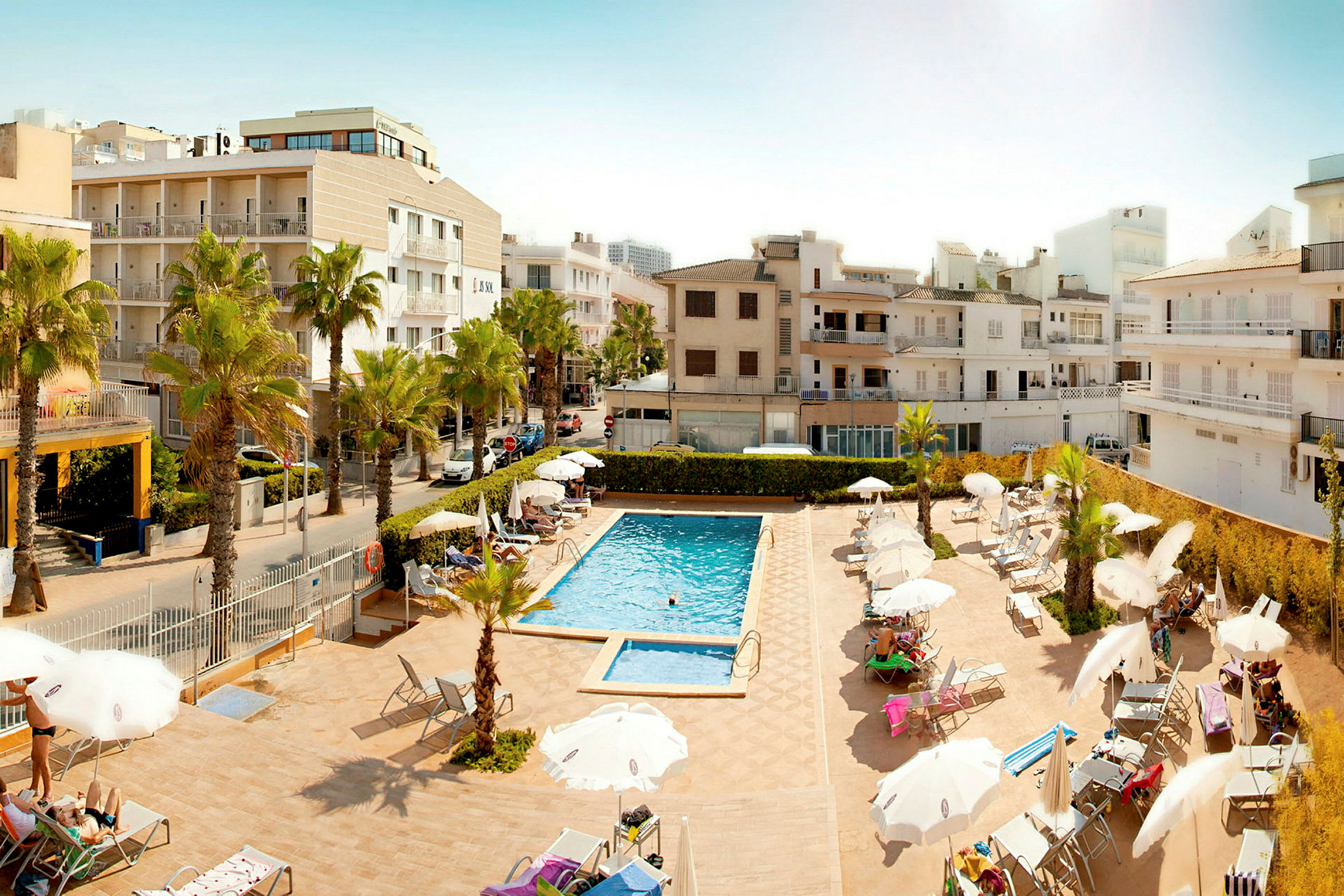 Hotellbassenget område med solsenger og parasoller omgitt av bygninger. (AI-generert tekst)