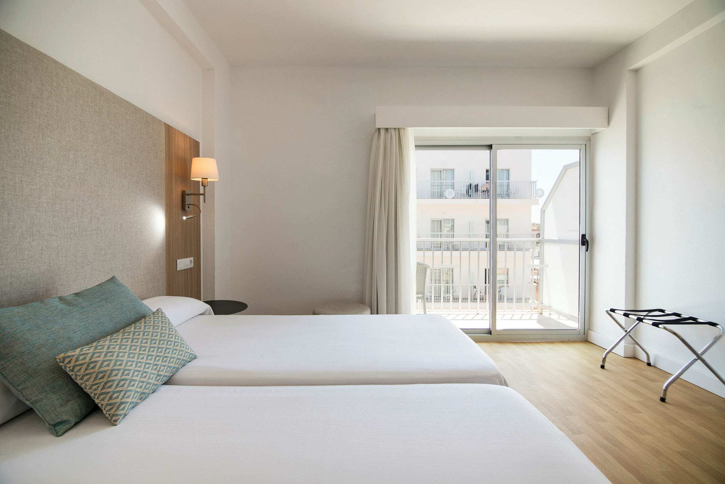 To enkeltsenger i et hotellrom med lys innredning og et vindu med balkong. (AI-generert tekst)