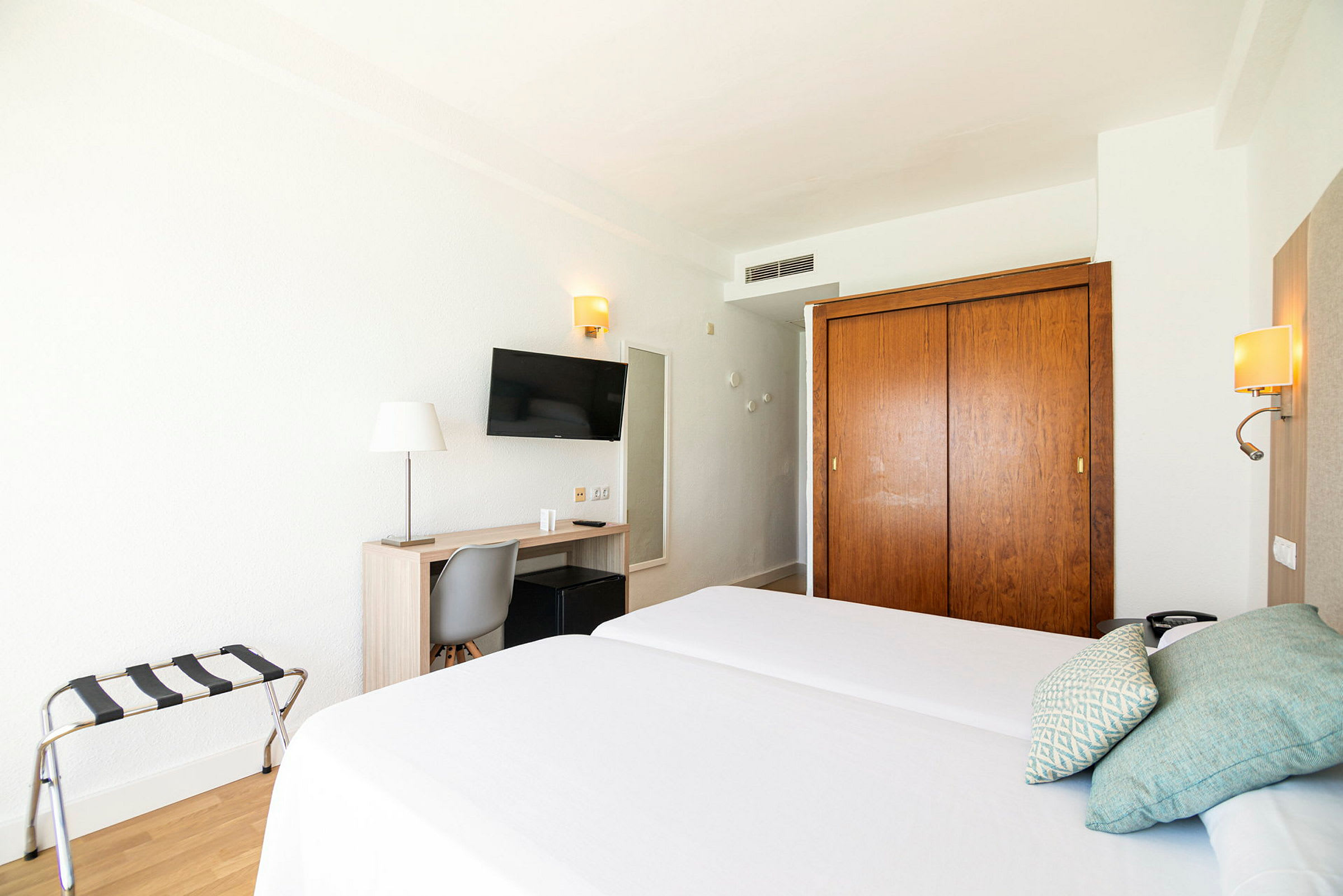 Hotellrom med to enkeltsenger, skrivebord, stol, TV og garderobeskap. (AI-generert tekst)