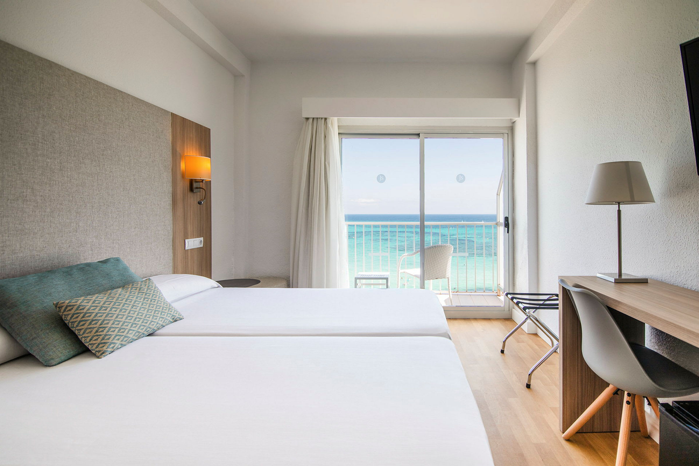 Hotellrom med to senger, skrivebord og utsikt over havet gjennom en glassdør. (AI-generert tekst)