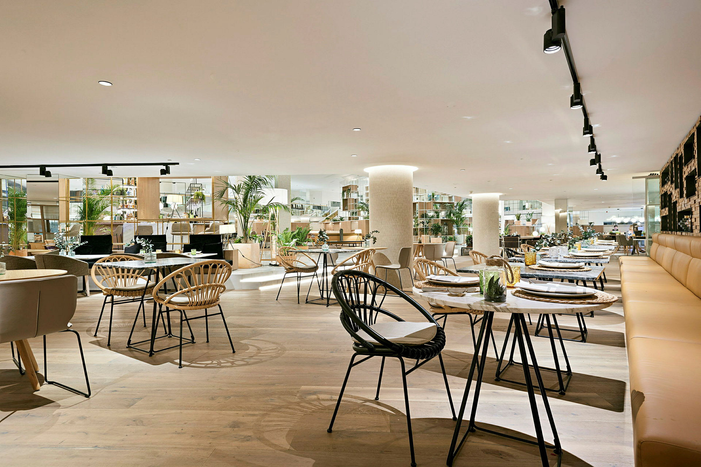 En romslig restaurant med moderne interiør, trebord og stoler samt grønne planter som dekorasjon. (AI-generert tekst)