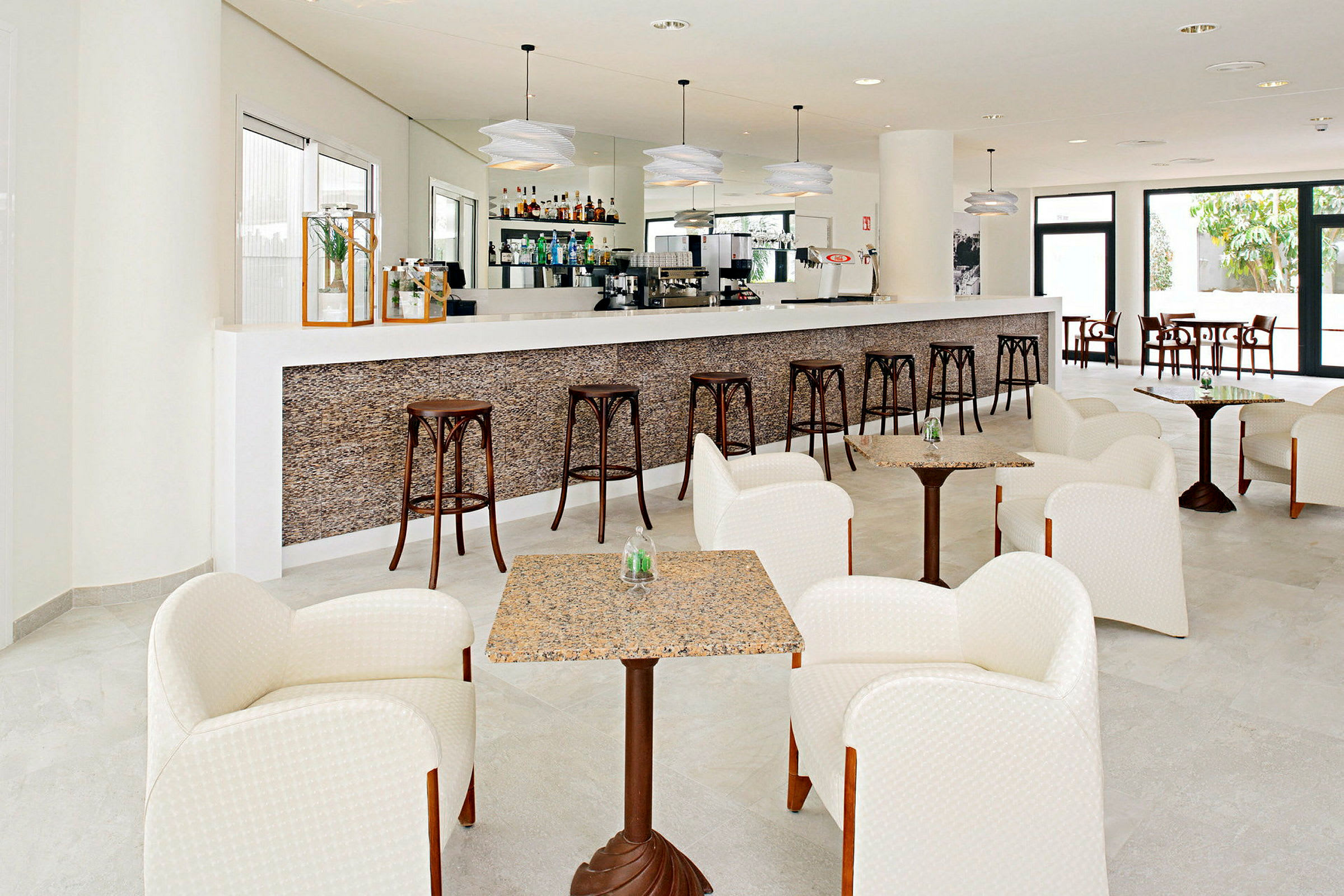 Bilde av en moderne hotellbar med en lang bardisk, høye barstoler og sittegrupper med lenestoler og små bord. (AI-generert tekst)