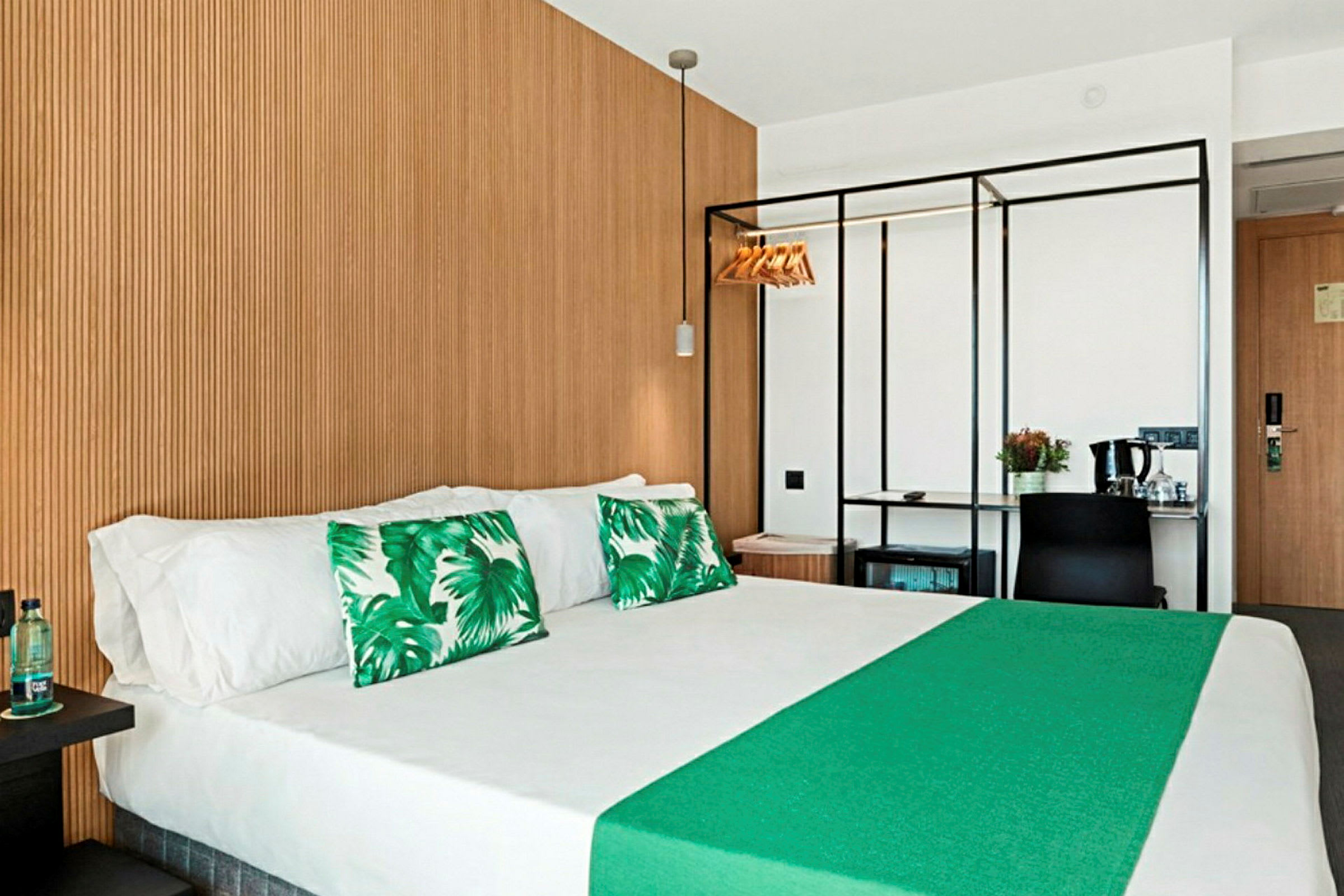 Hotellrom med dobbeltseng, grønne dekorasjonsputer og trepanel på veggen. (AI-generert tekst)