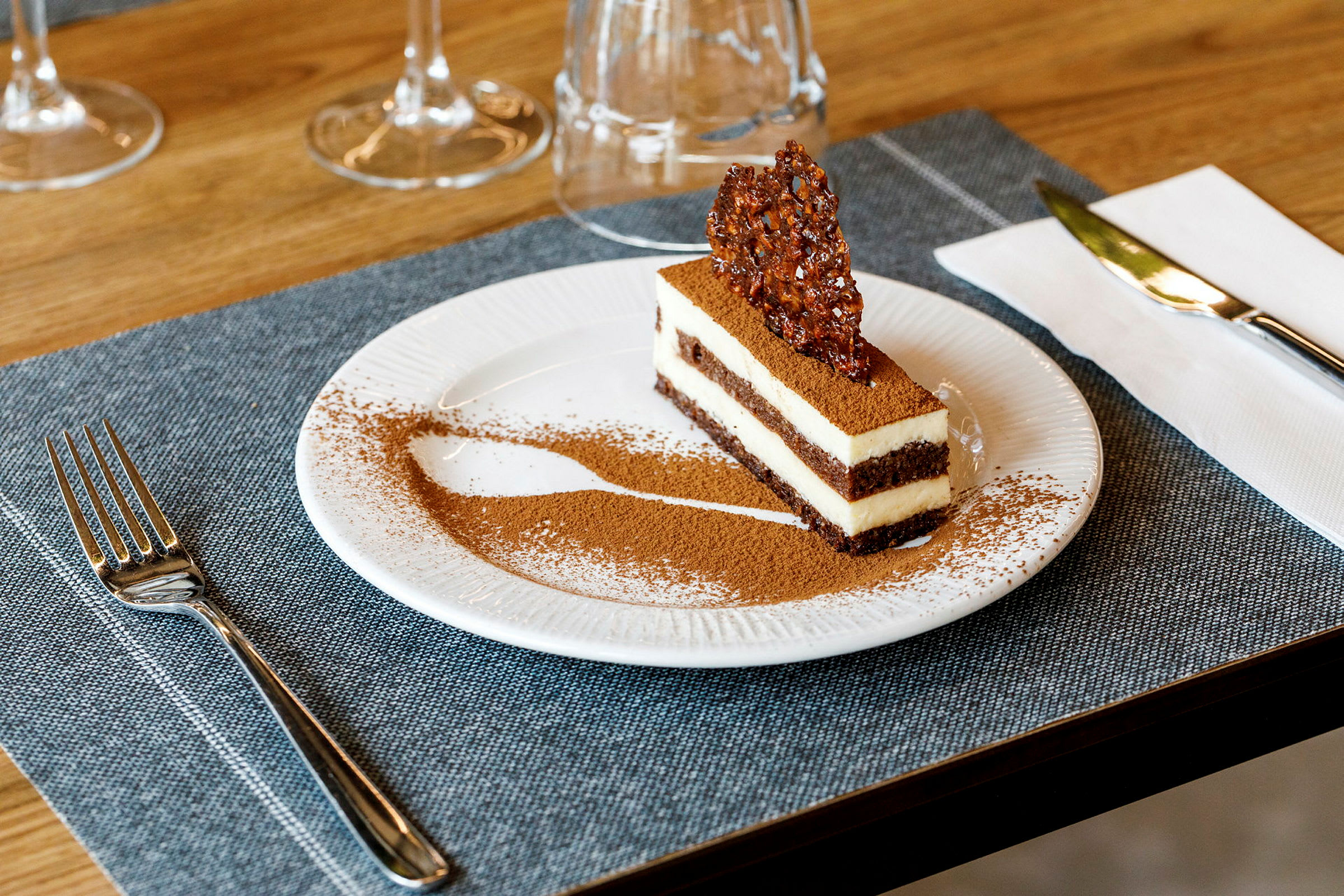En dessert, sannsynligvis en tiramisu, servert på en tallerken, dekorert med kakaopulver og et sprøtt karamellstykke på toppen. (AI-generert tekst)