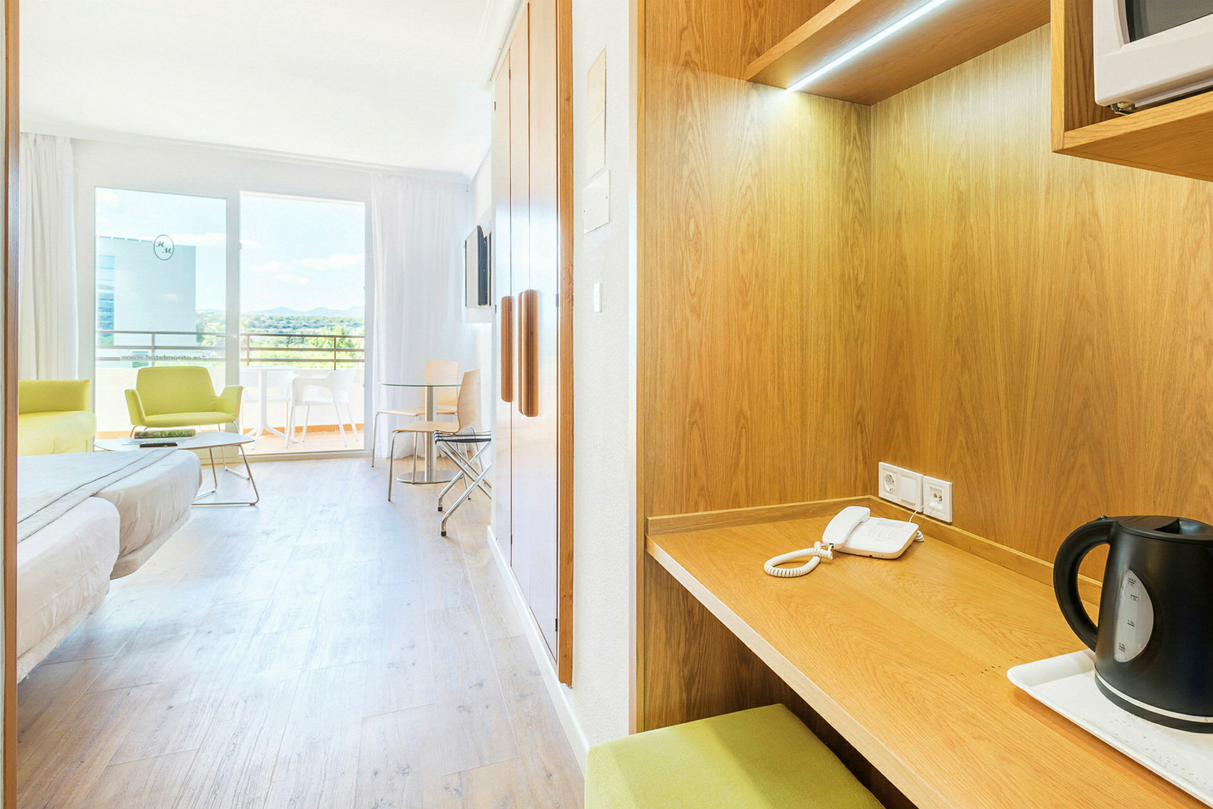 Et hotellrom med enkeltseng, sittegruppe, skrivebord og bord ved en balkong. (AI-generert tekst)