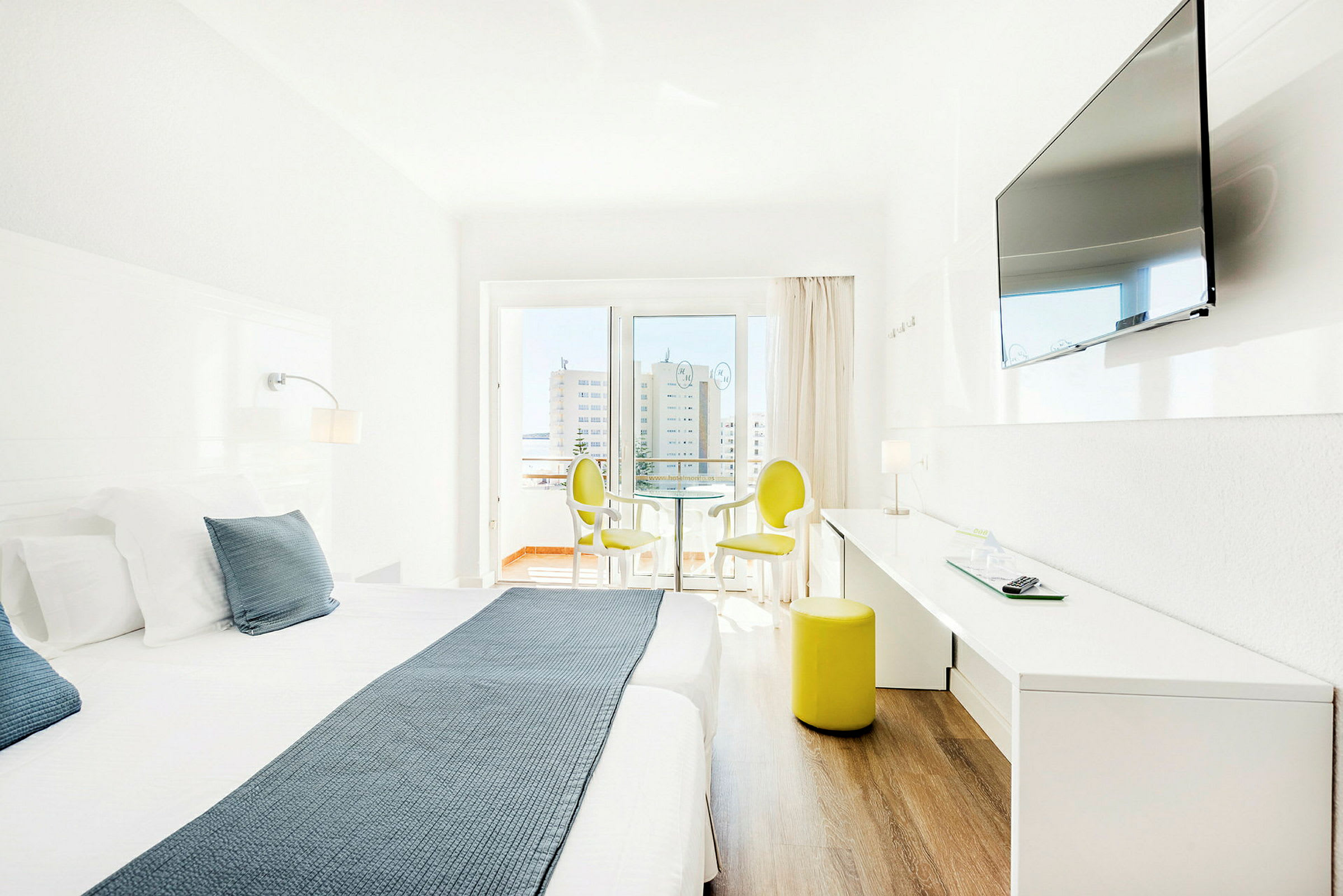 Lyst hotellrom med dobbeltseng, TV på veggen og sittemøbler ved vinduet. (AI-generert tekst)