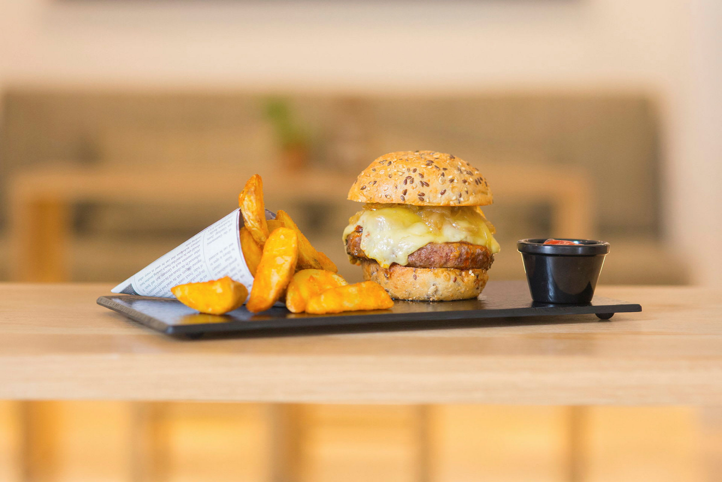 Burger med ost, potetbåter og dipp på en tallerken. (AI-generert tekst)