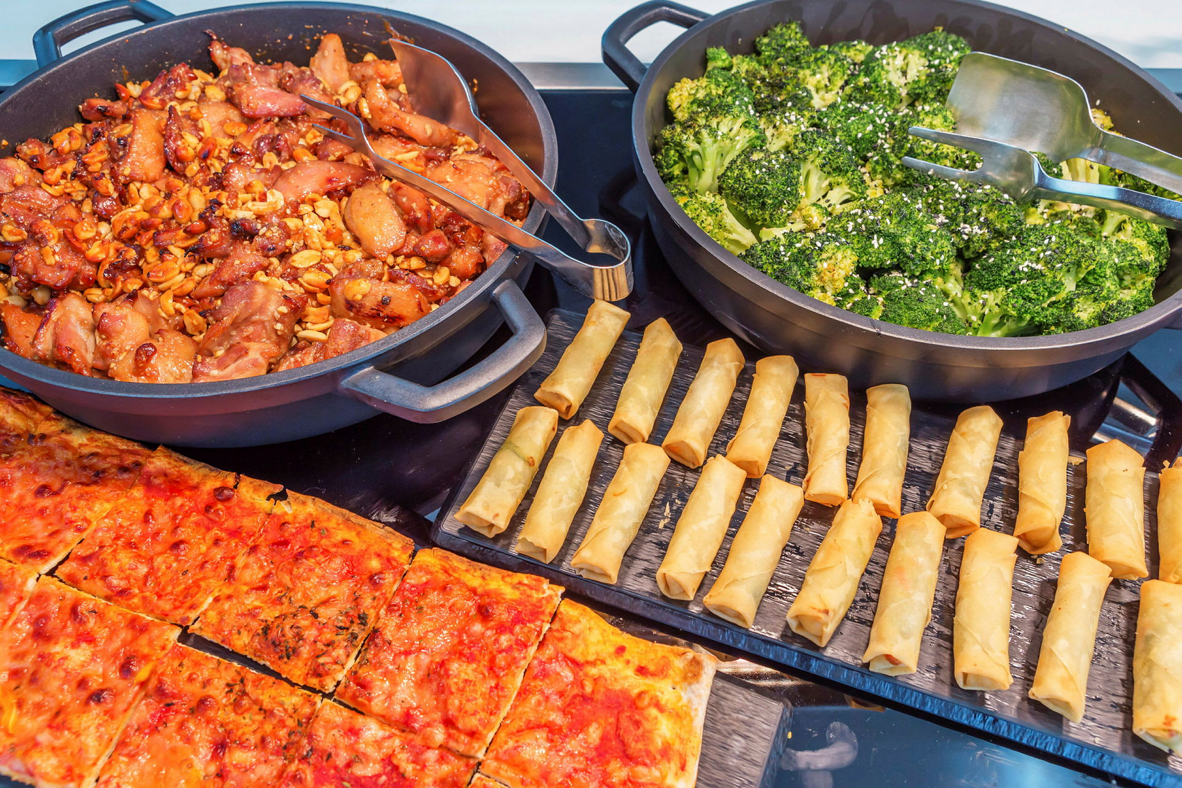 En buffé med forskjellige retter, inkludert kylling, brokkoli, vårruller og pizza. (AI-generert tekst)