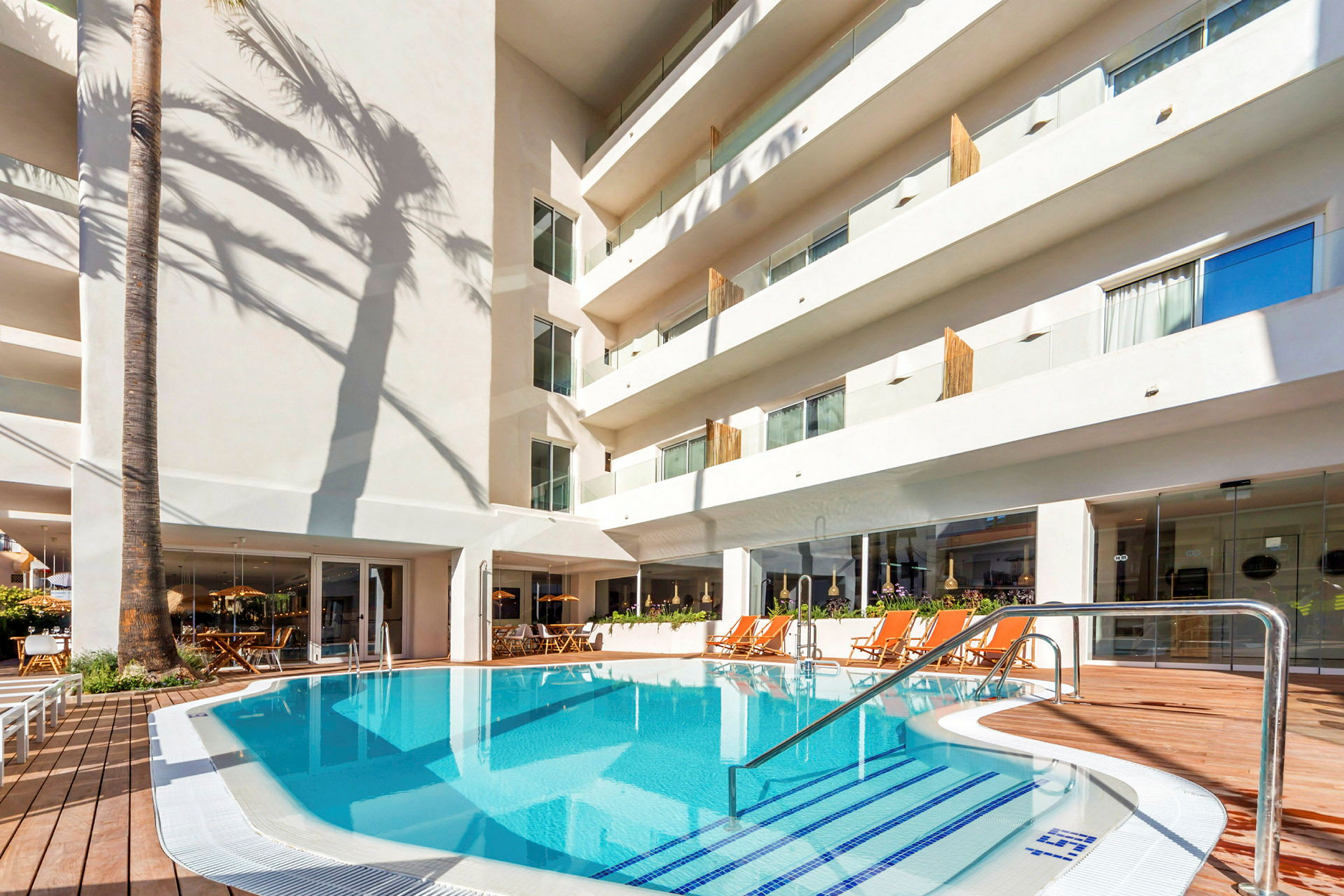 Et hotellbasseng omgitt av solsenger og en hvit bygning. (AI-generert tekst)