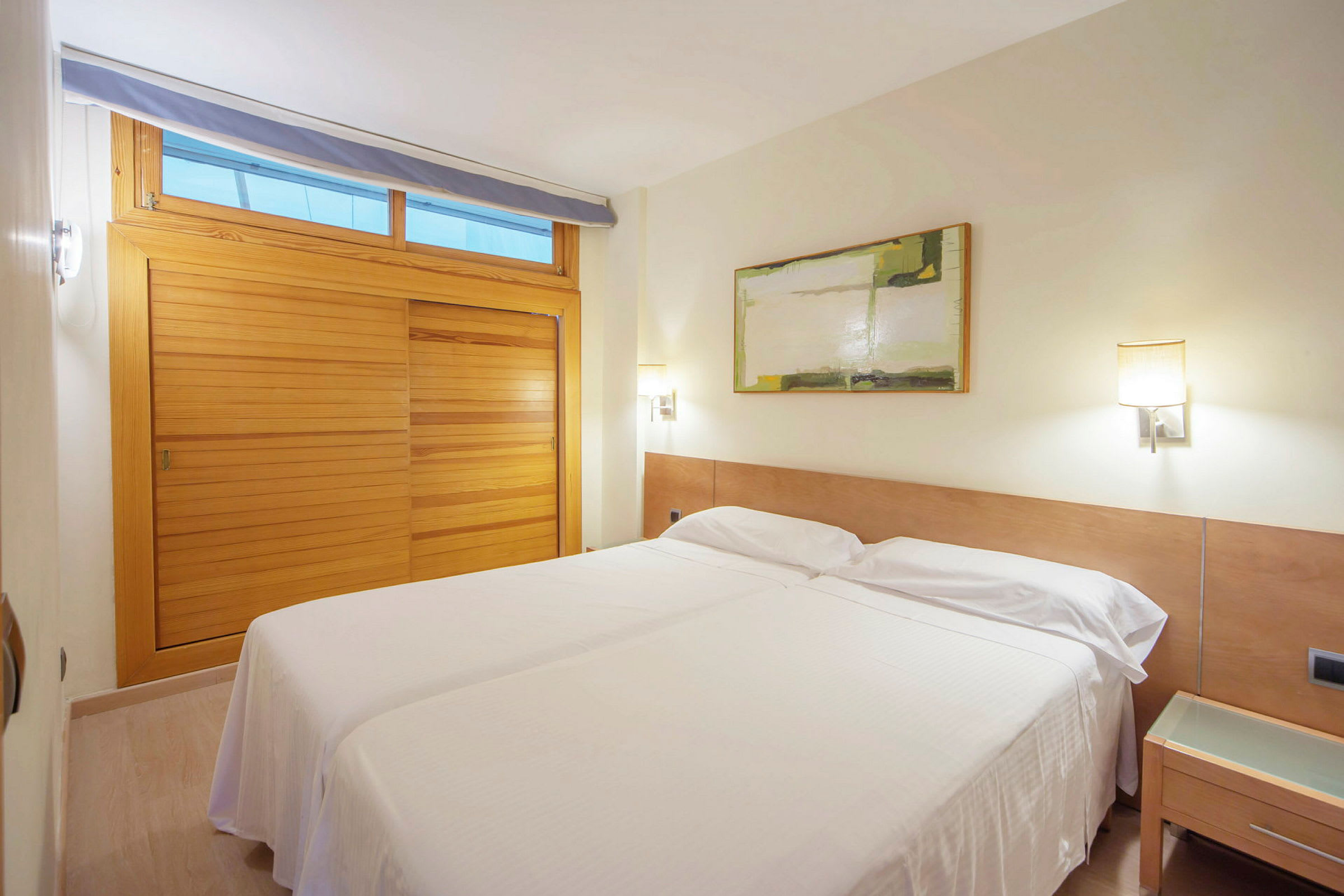Et hotellrom med to enkeltsenger plassert sammen, en trevegg og et maleri på veggen. (AI-generert tekst)