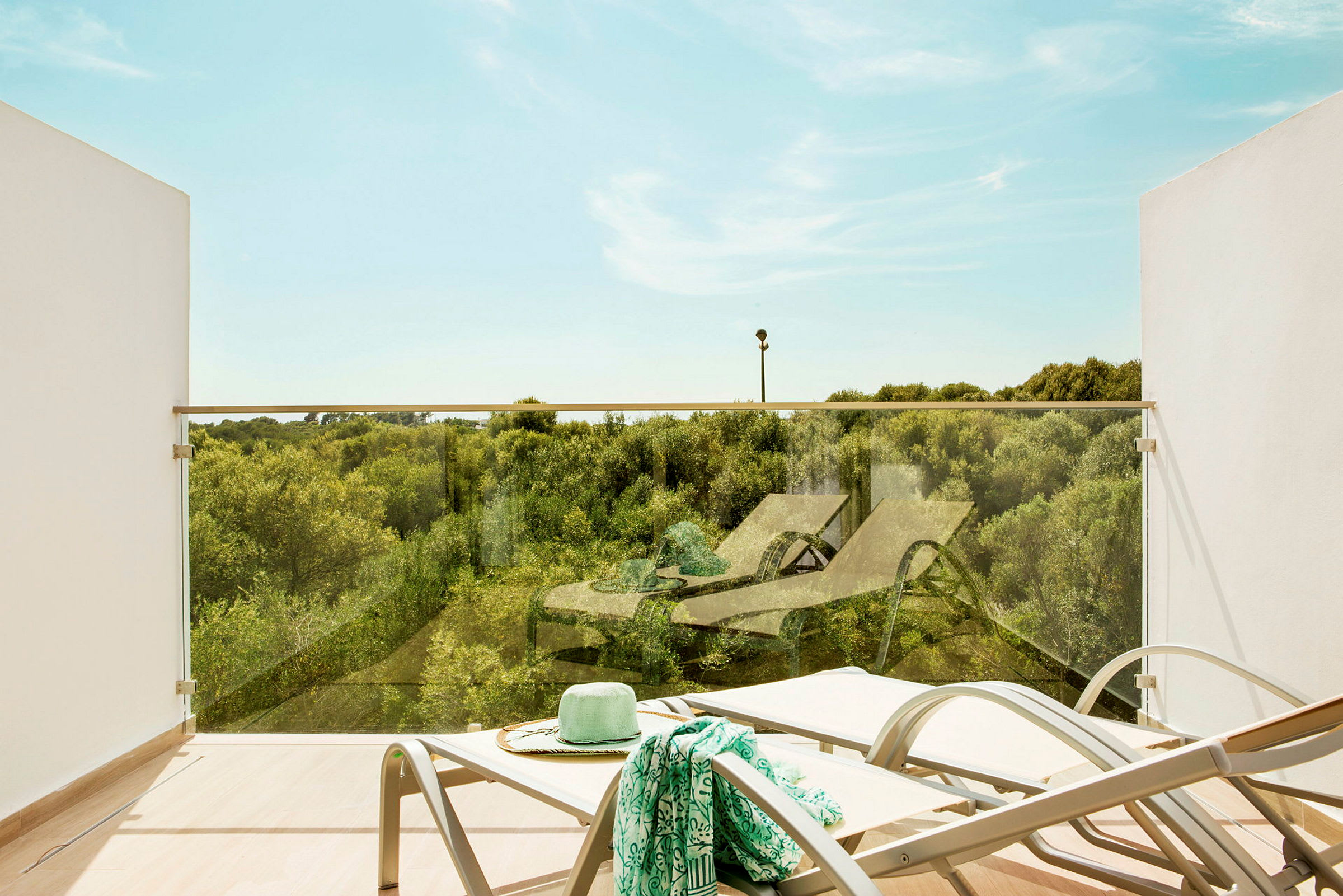 En terrasse med utsikt over grøntområder, solsenger og rekkverk av glass. (AI-generert tekst)