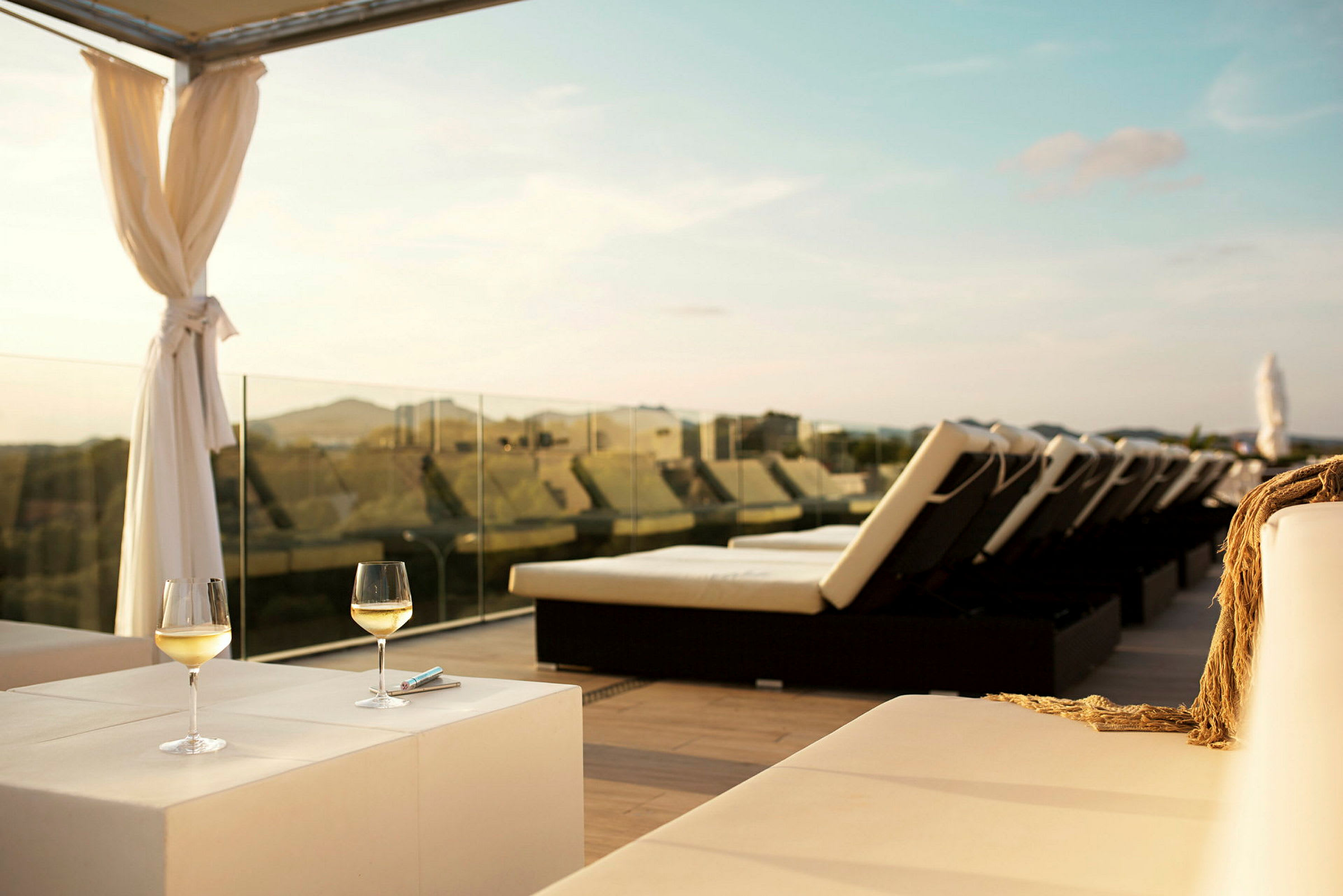 Solterrasse med solsenger, to glass hvitvin på et bord og utsikt over landskapet. (AI-generert tekst)