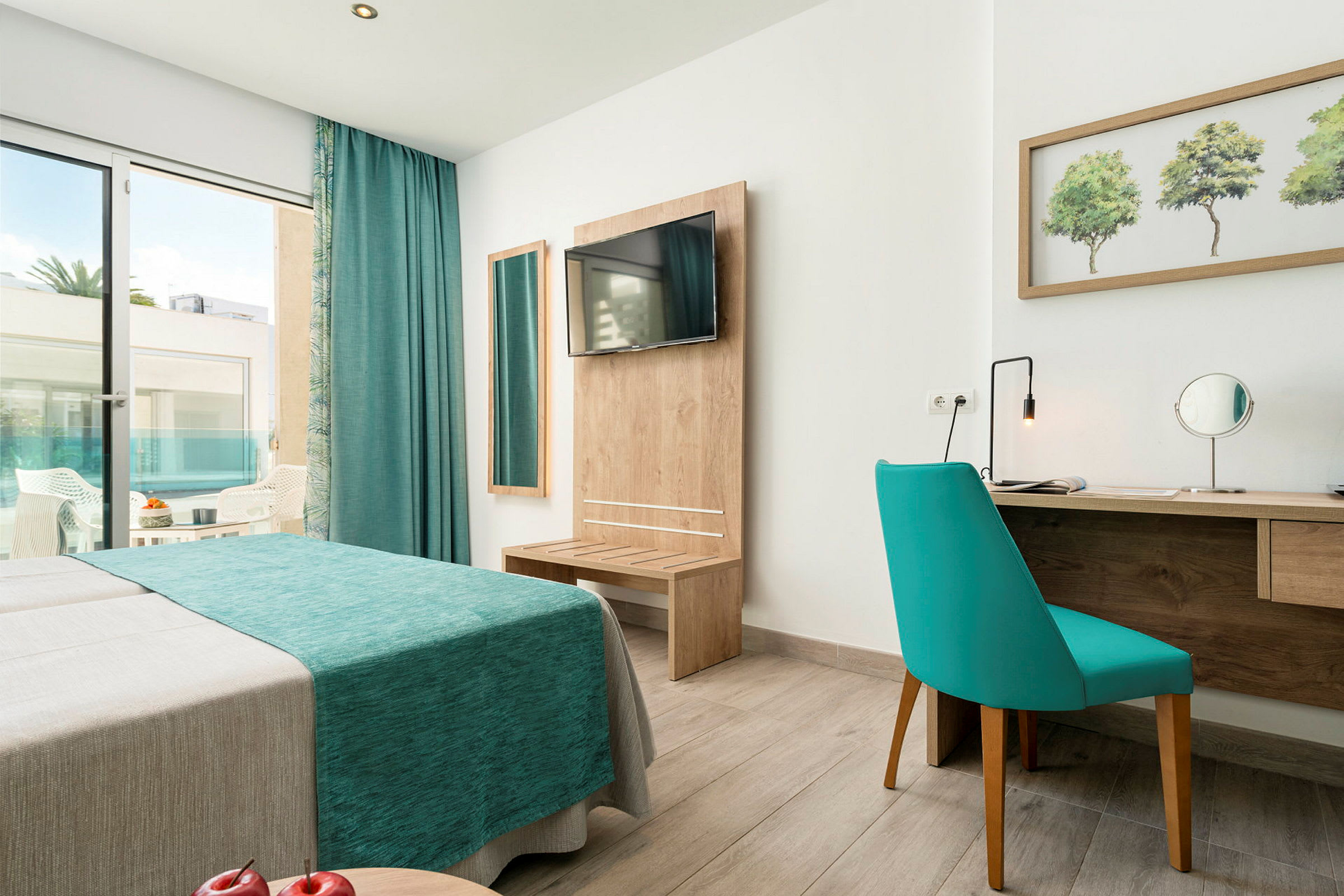 Et hotellrom med en blå sofa, speil, skrivebord og en utgang til en balkong. (AI-generert tekst)