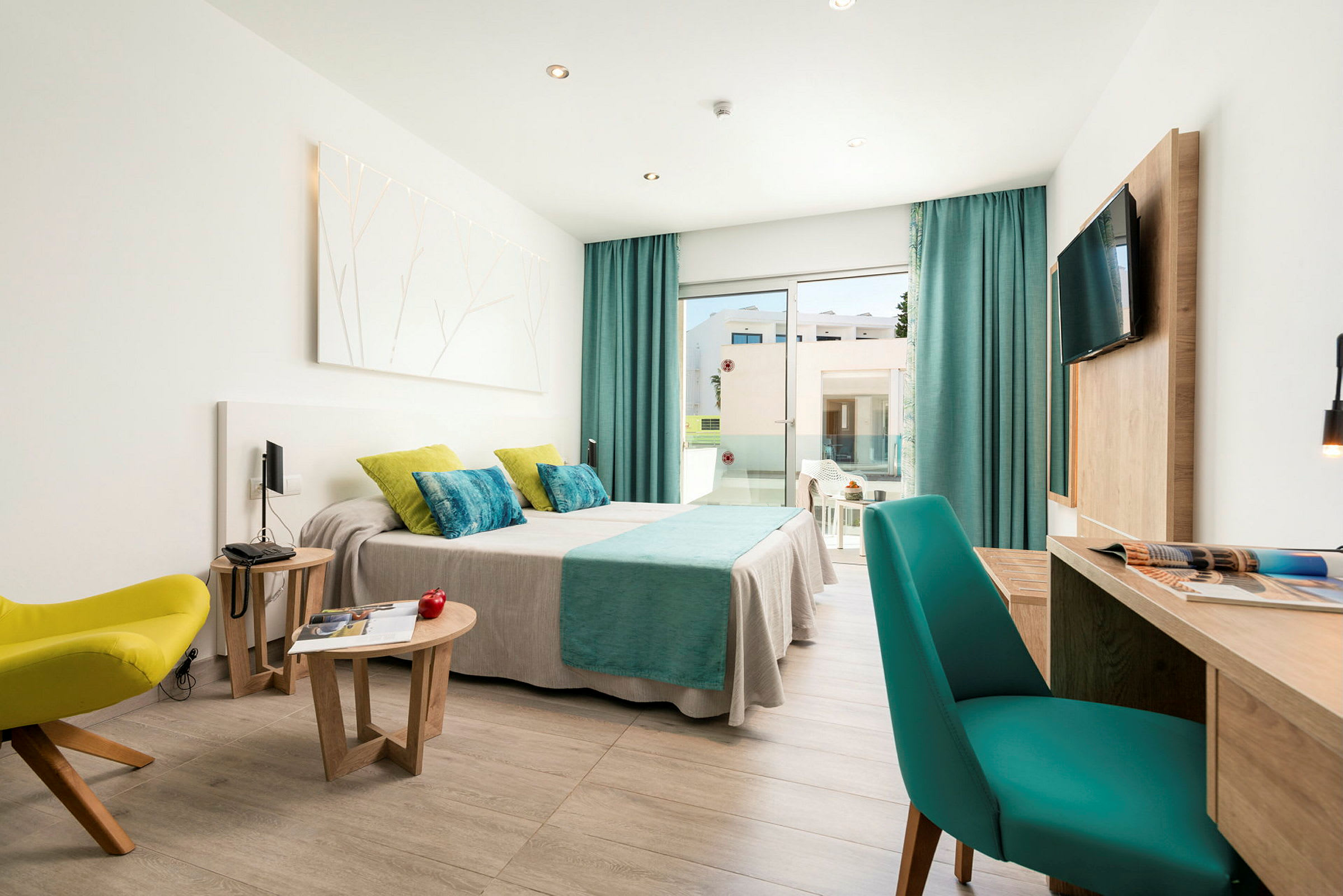 Et moderne hotellrom med en dobbeltseng dekket med skarpe tekstiler, sitteplasser og et skrivebord. Vinduer fører til en balkong. (AI-generert tekst)
