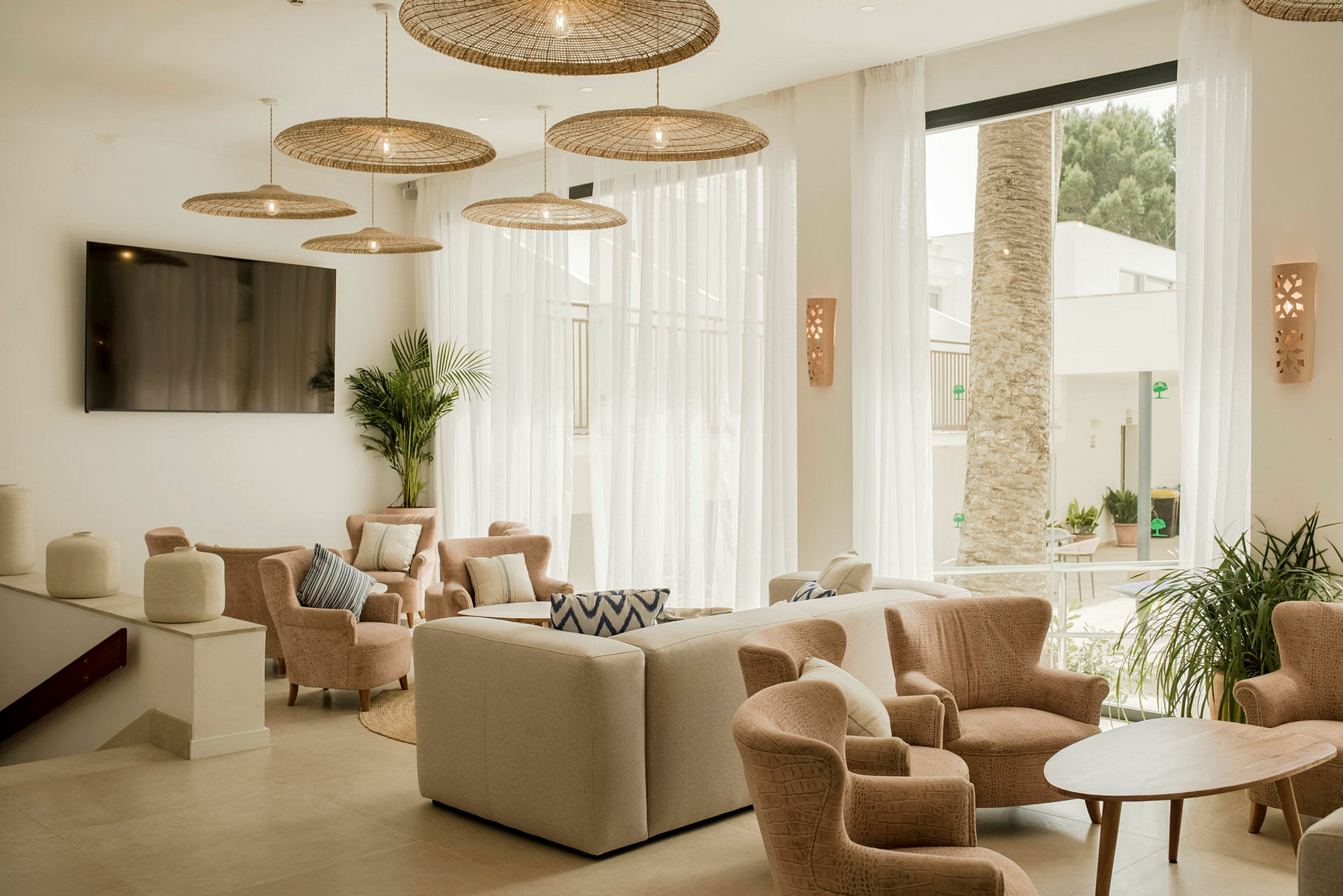 Et lyst og elegant stueområde med stoler og sofa rundt et trebord, samt store vinduer med utsikt mot palmer utendørs. (AI-generert tekst)