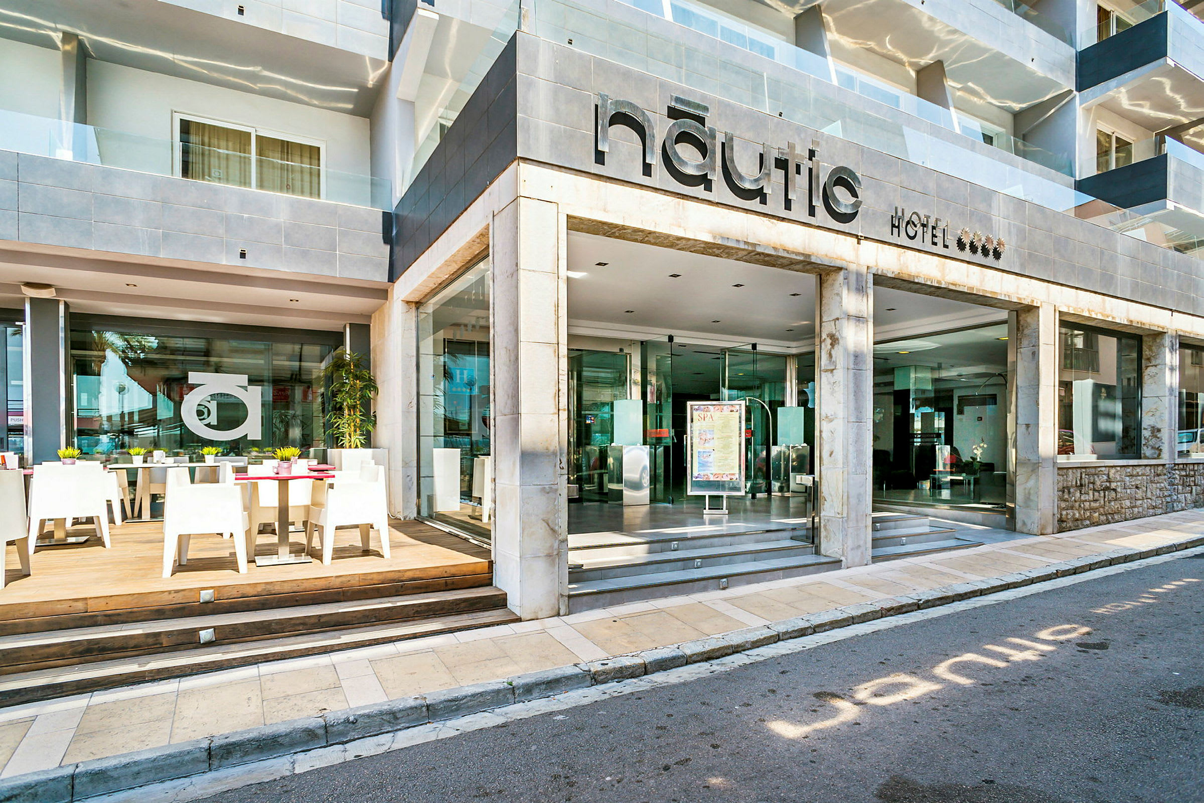 Hotel Nautics inngang og utendørs servering med bord og stoler. (AI-generert tekst)