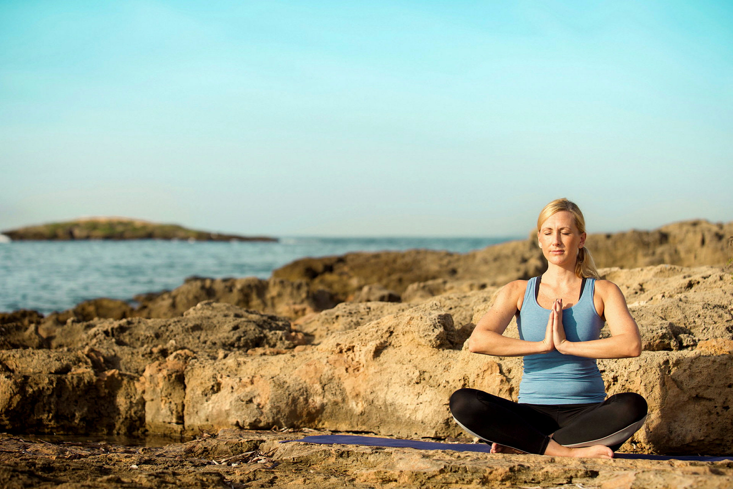 Person i treningsklær sitter i meditasjonsstilling på en klippe ved havet. (AI-generert tekst)