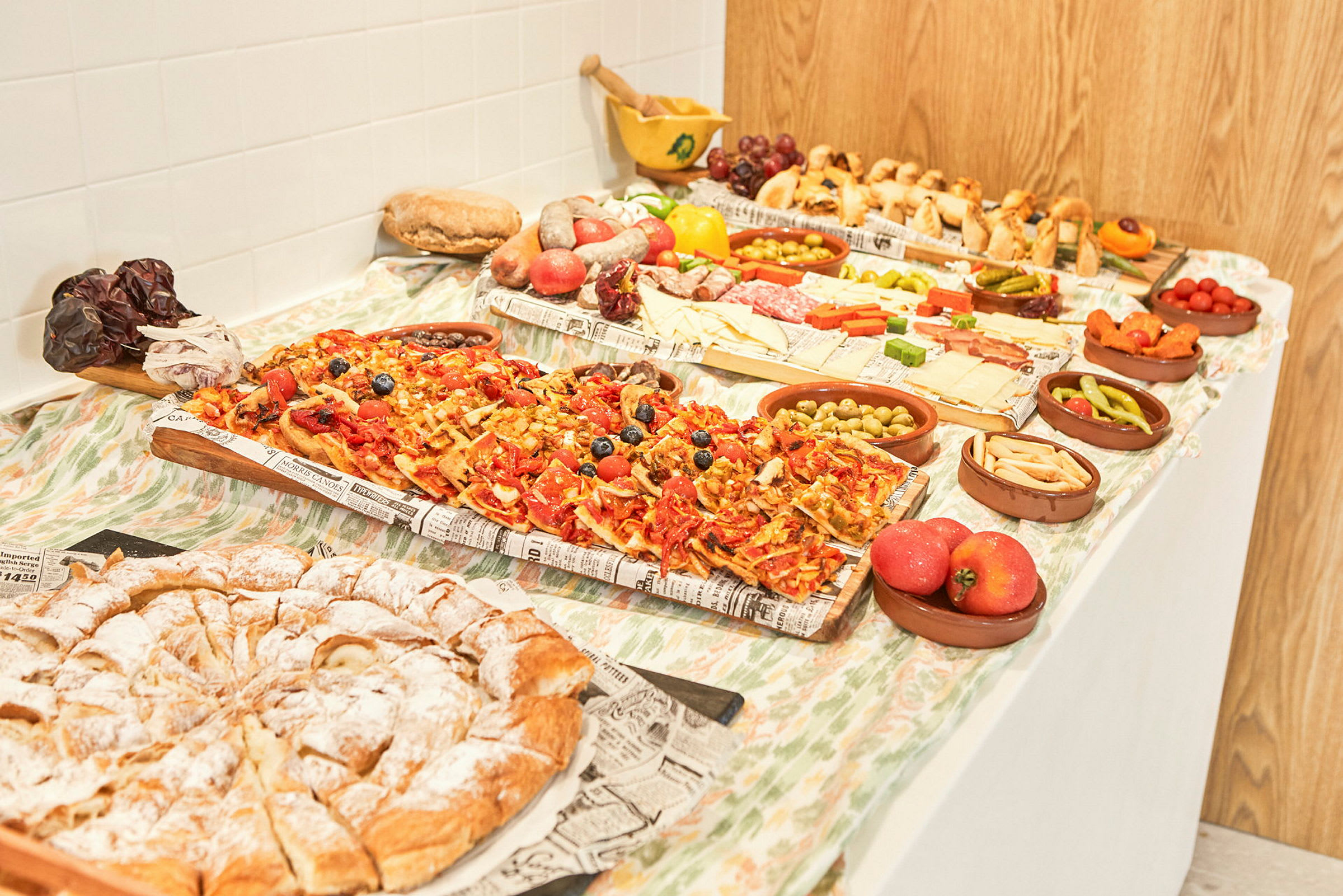 Et bord dekket med ulike matvarer som pizzastykker, bakverk, ost, frukt og grønnsaker. (AI-generert tekst)