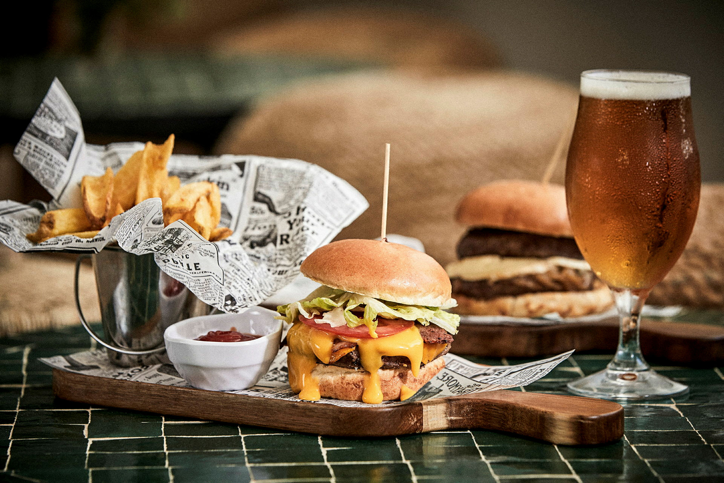 En hamburger, pommes frites og et glass øl på et bord. (AI-generert tekst)