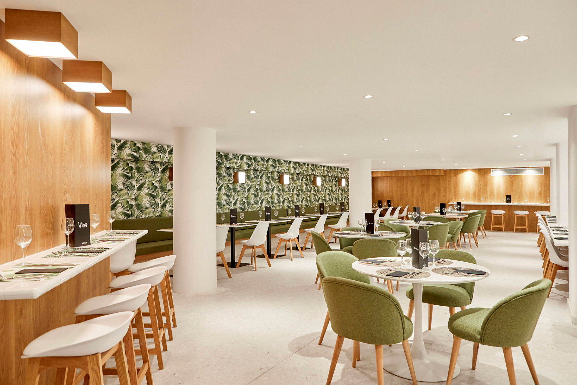Et restaurantinteriør med grønmalte stoler og en tapetert vegg med planteprint. (AI-generert tekst)