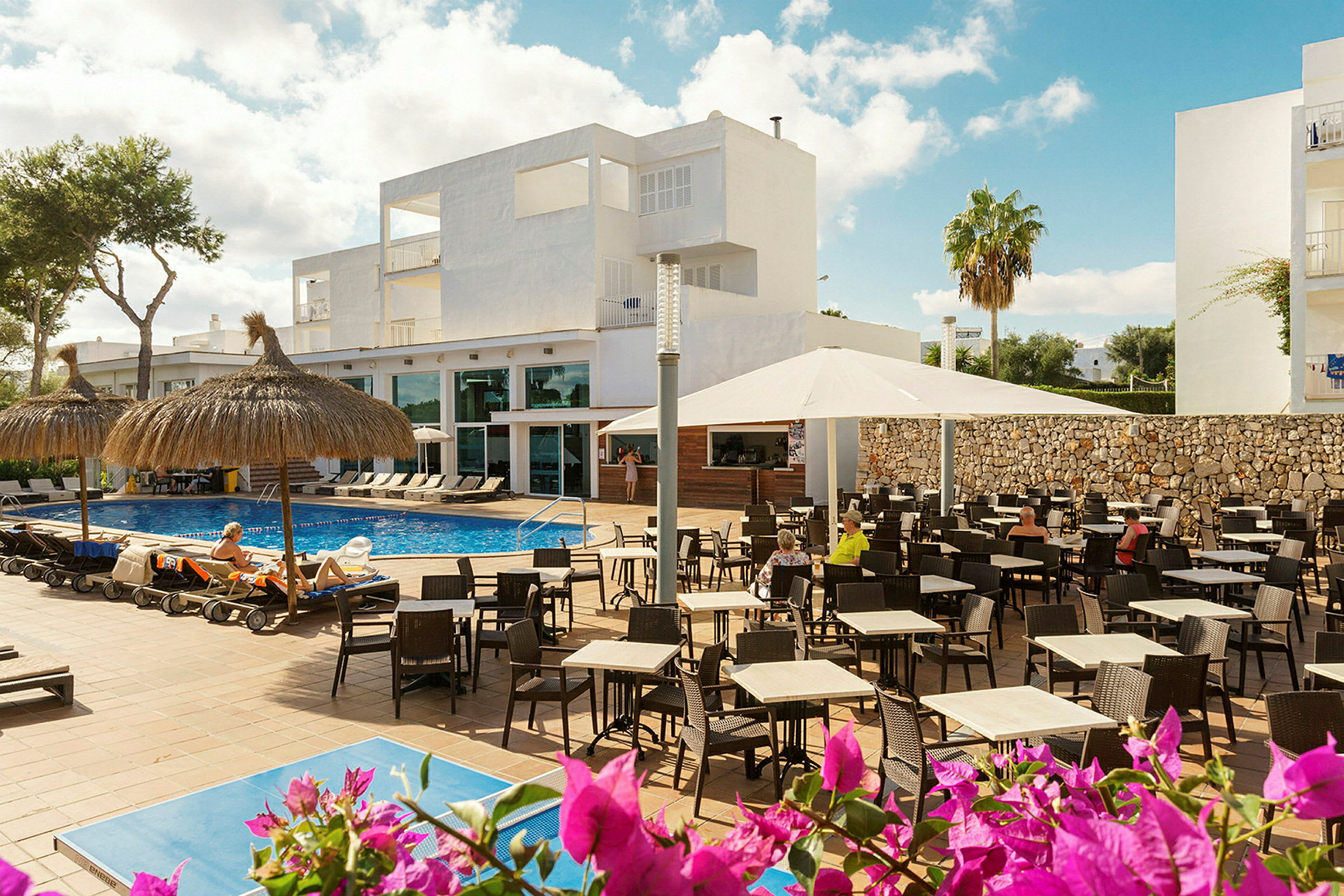 En hotellinnretning med bassengområde, solsenger og utendørs bord. (AI-generert tekst)