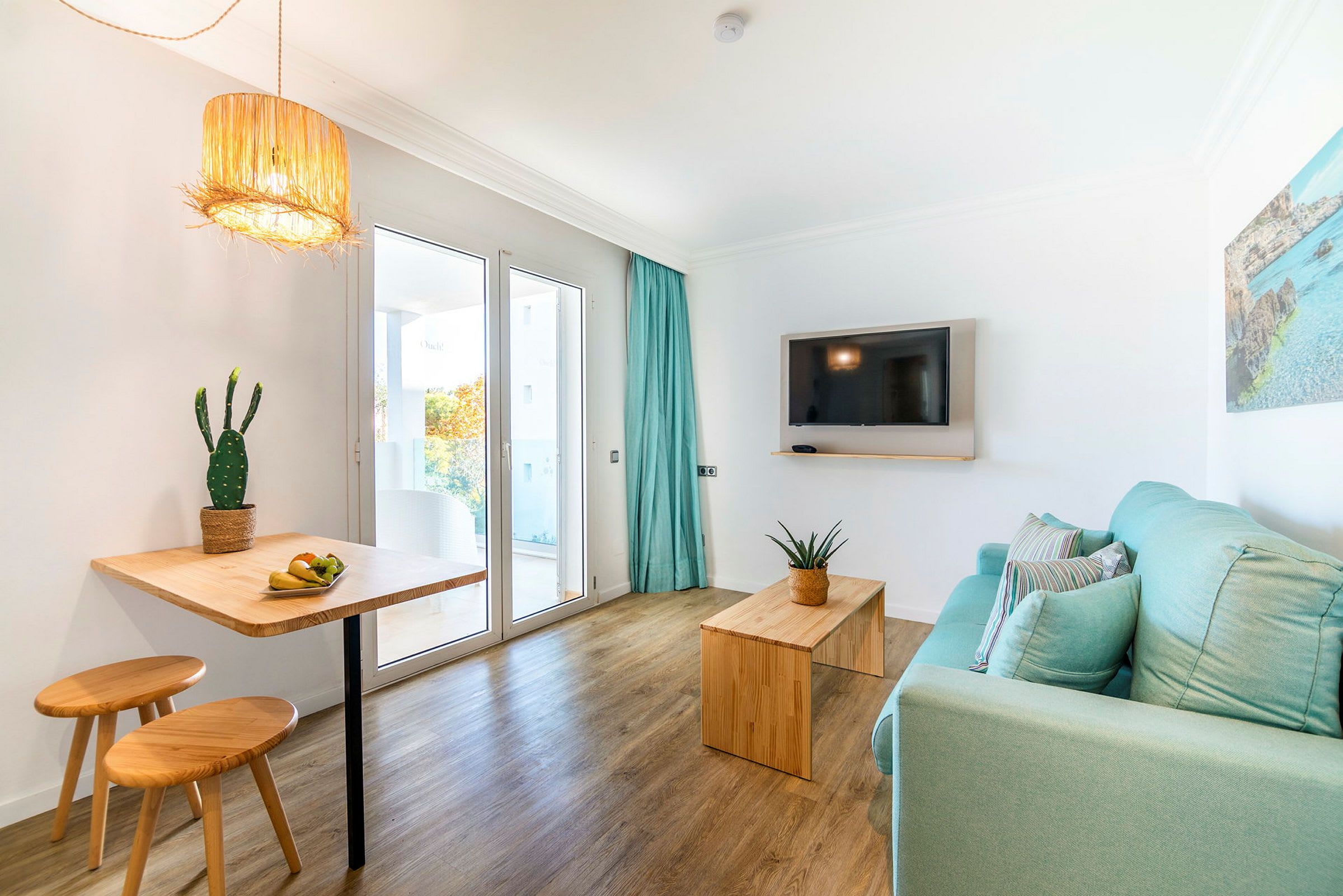 Lyst og moderne interiør med trebord, stoler, turkis sofa, og en TV på veggen med utsikt mot en balkong. (AI-generert tekst)