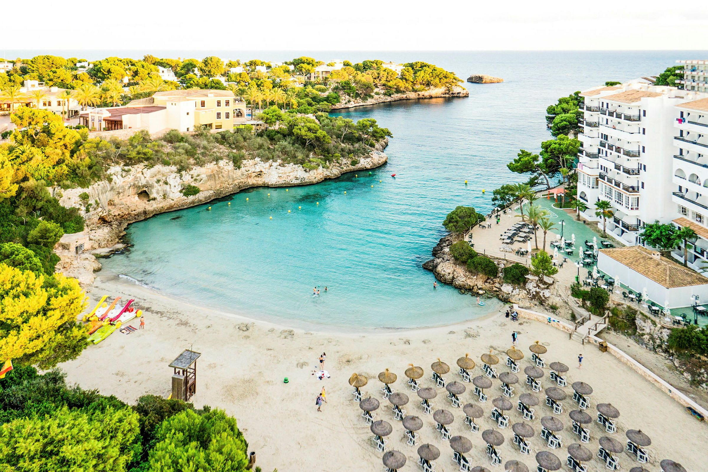 Strand med parasoller og solsenger ved en turkis bukt omgitt av klipper og vegetasjon. (AI-generert tekst)