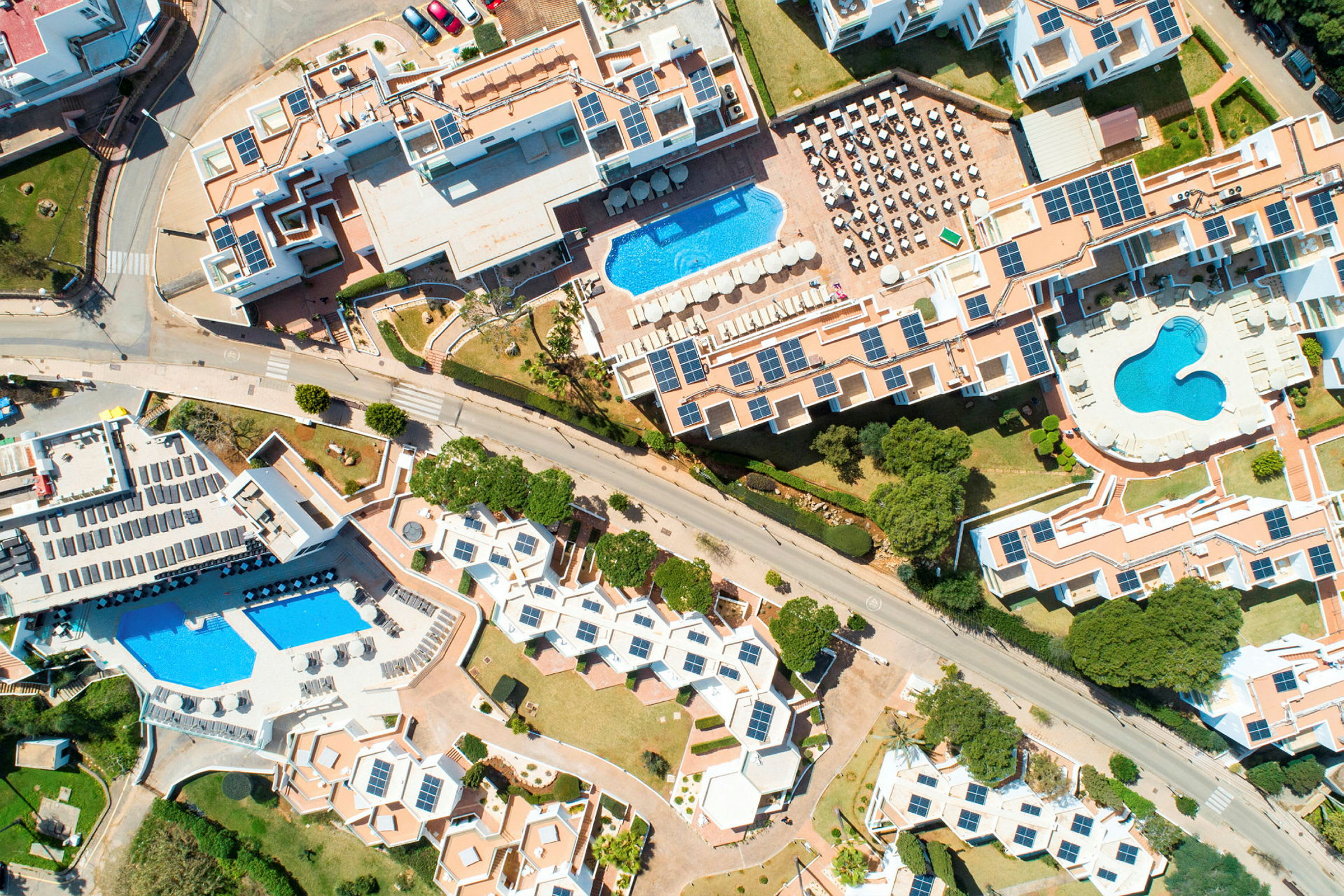 Luftfoto av et hotellområde med bassenger og solcellepaneler. (AI-generert tekst)