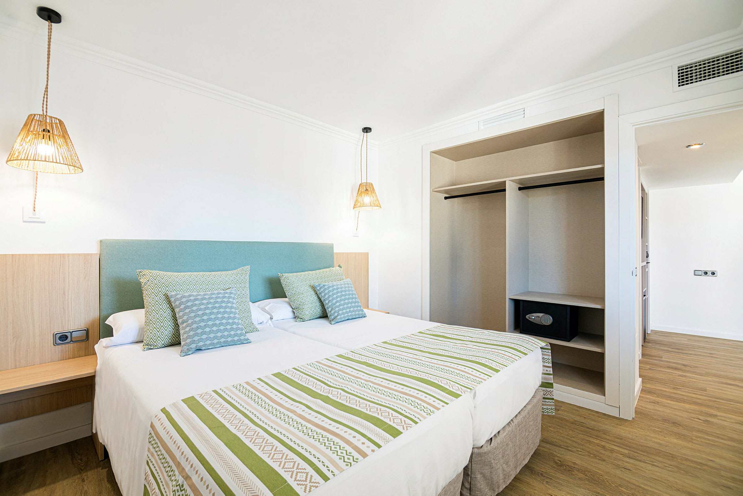 Et hotellrom med en dobbeltseng, sengelamper og en åpen garderobe. (AI-generert tekst)