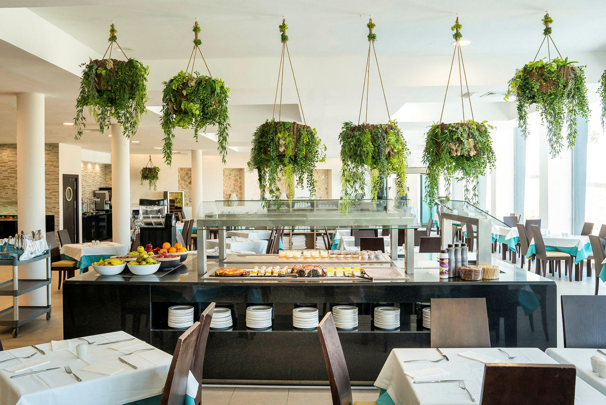 Restaurant med bord, stoler og buffet samt hengende grønne planter. (AI-generert tekst)
